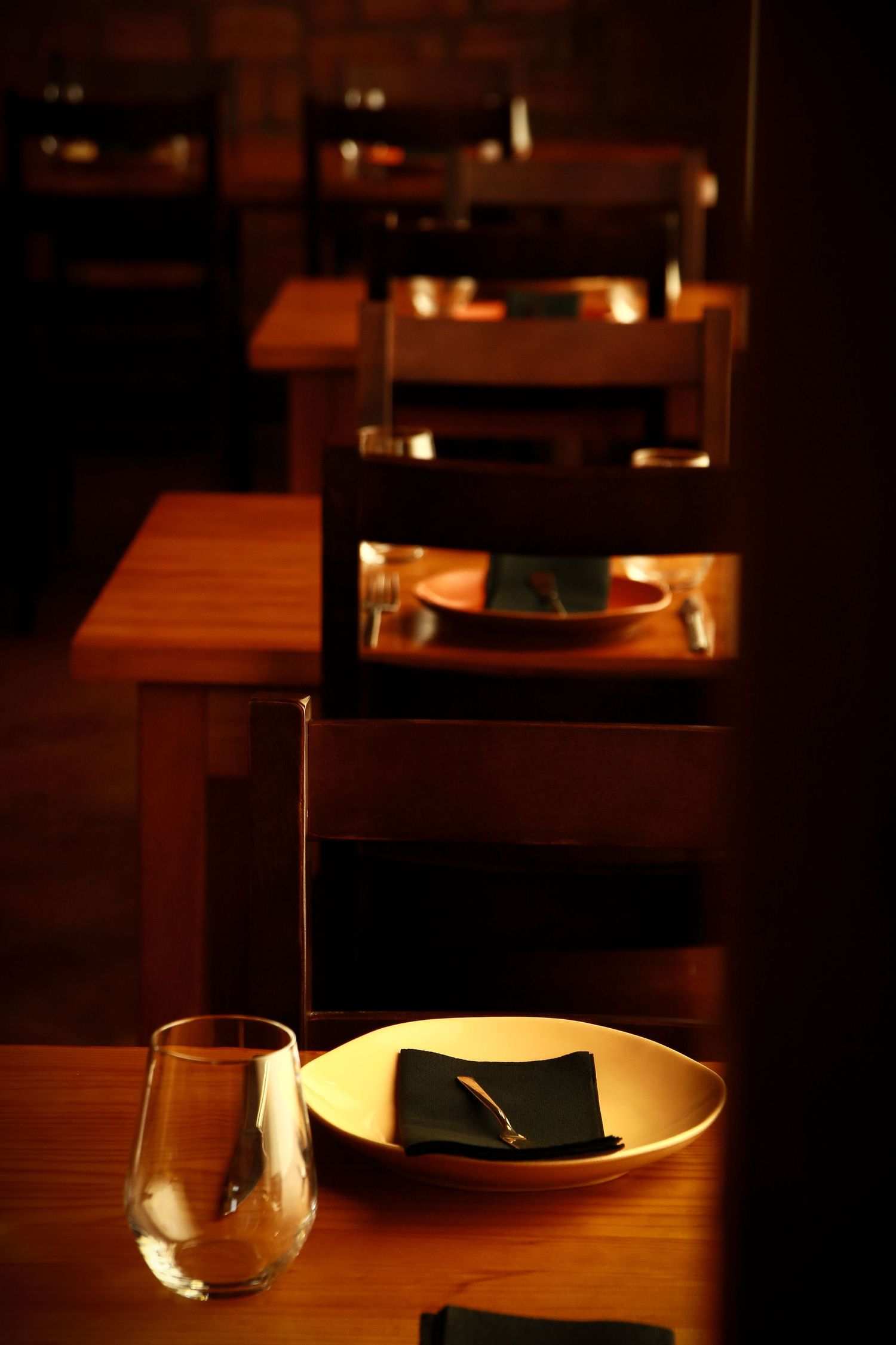 Restaurant table setting with wine glass and plate in intimate lighting.