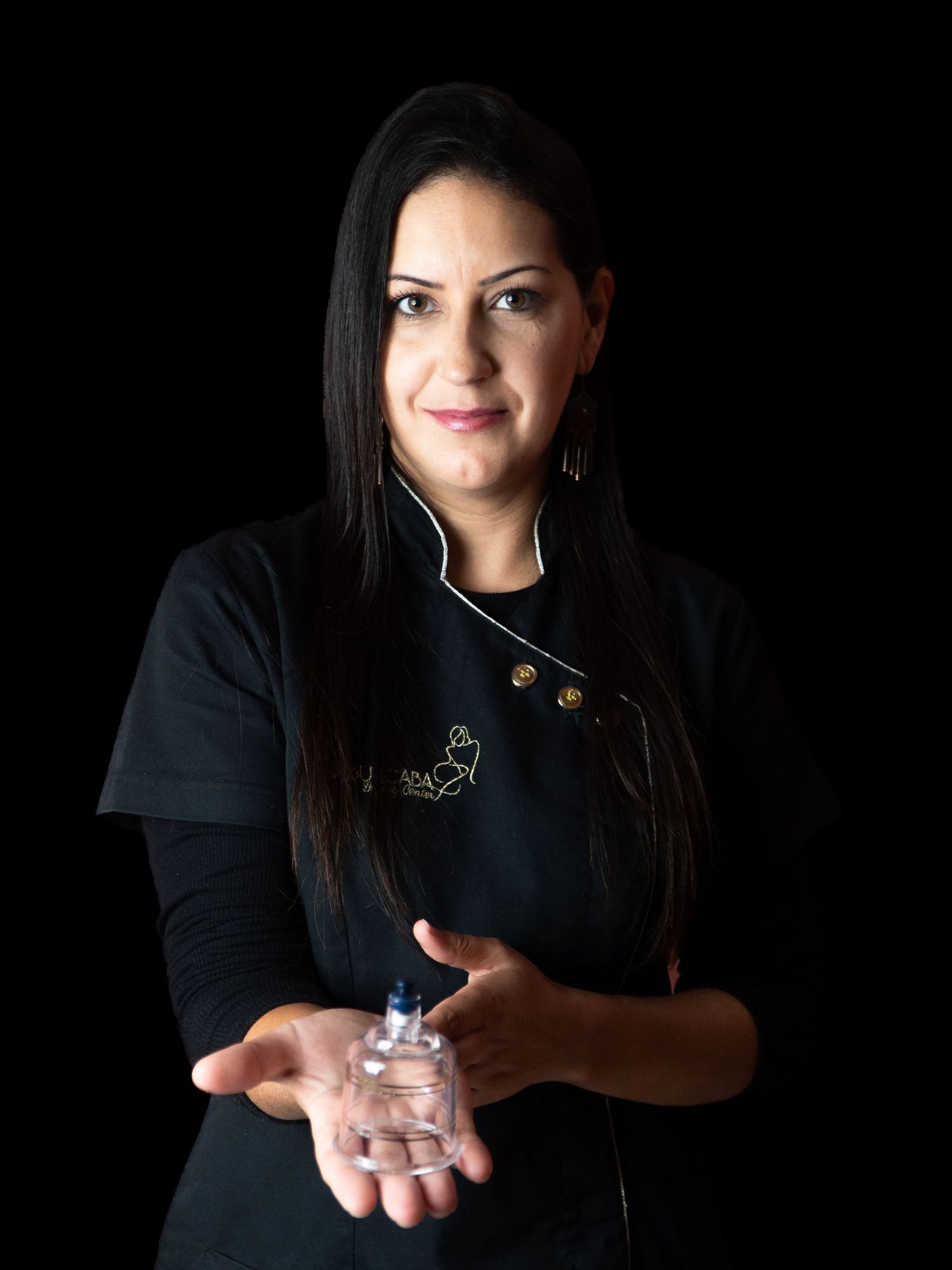 Beauty professional in black chef-style uniform holding small glass container.