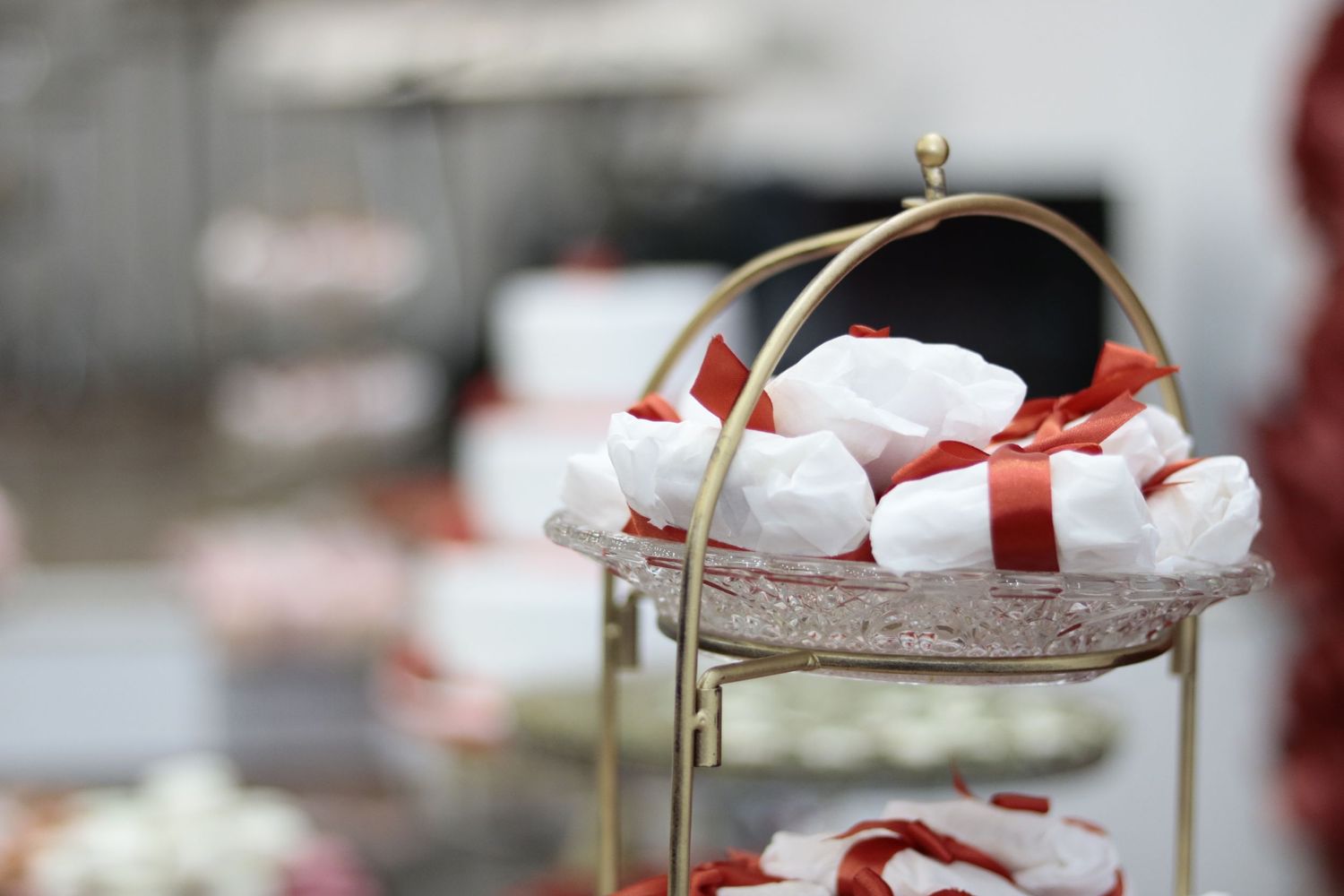 Small white favor boxes with red ribbons displayed on an elegant tiered serving stand.