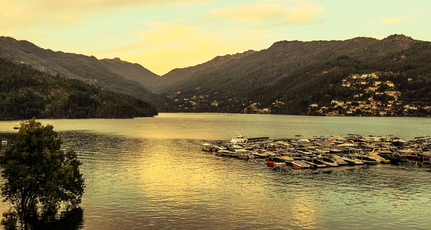 Golden sunset illuminates mountains and lake with wooden boat docks along the tranquil shoreline.