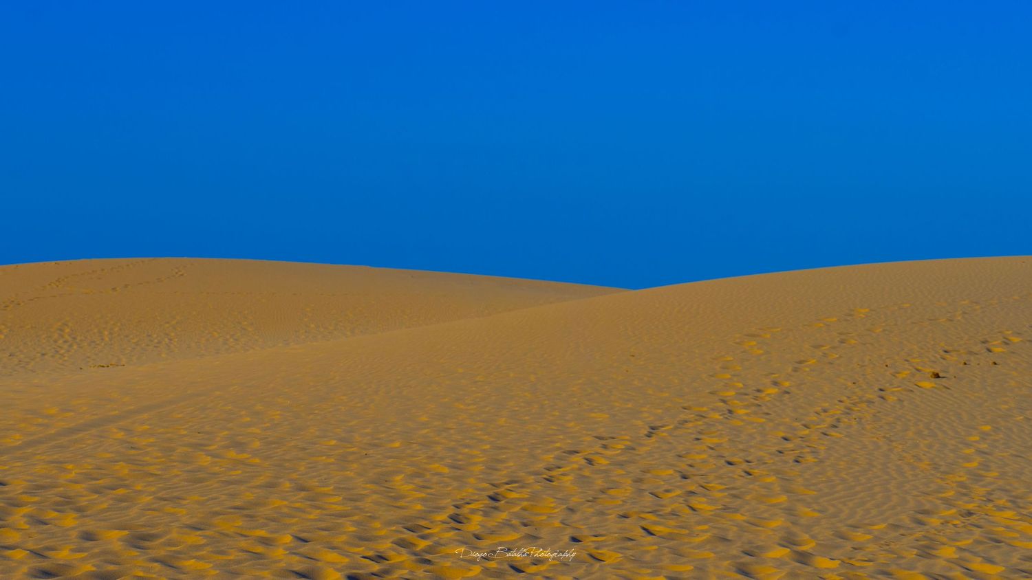 Minimalist landscape of golden sand dunes against deep blue sky.