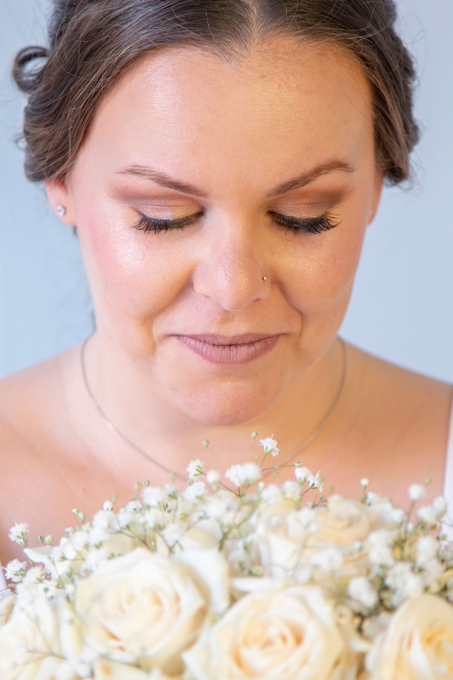 Close-up portrait with soft makeup and peach roses with baby's breath bouquet.