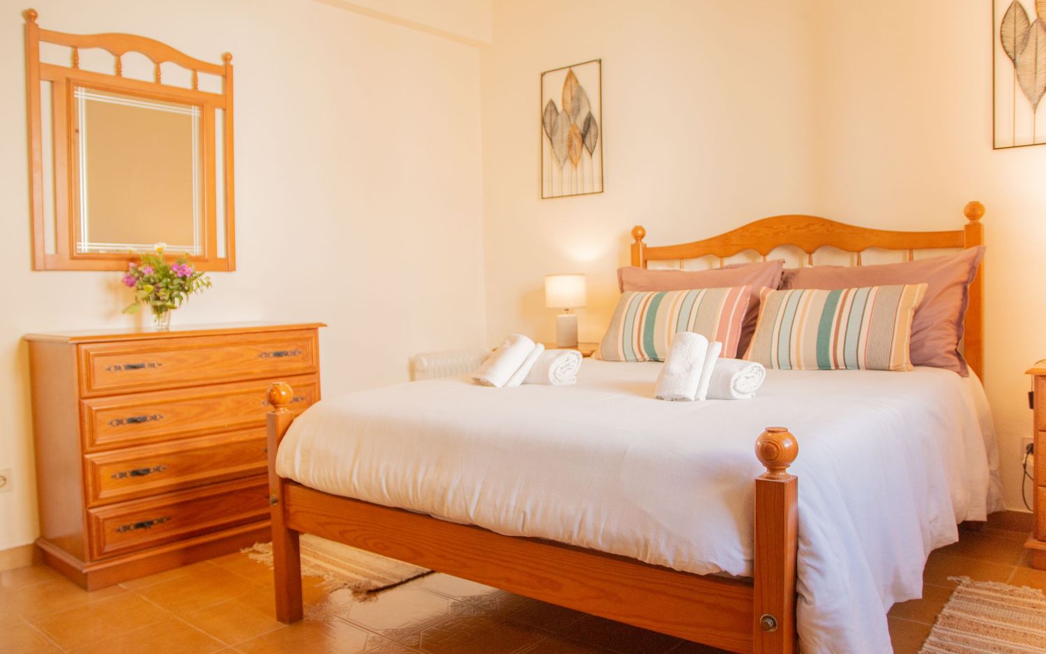 Bright bedroom with wooden pine furniture featuring a cozy double bed, striped linens, and matching dresser with mirror.