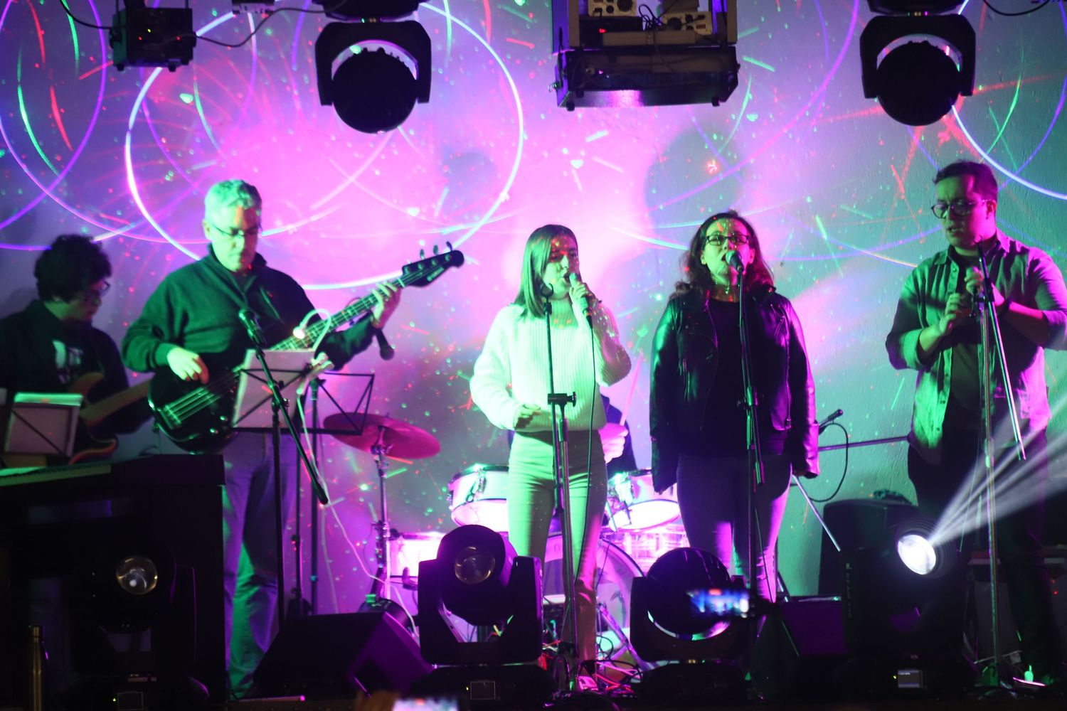 Band performing on stage with colorful pink and purple lighting effects.