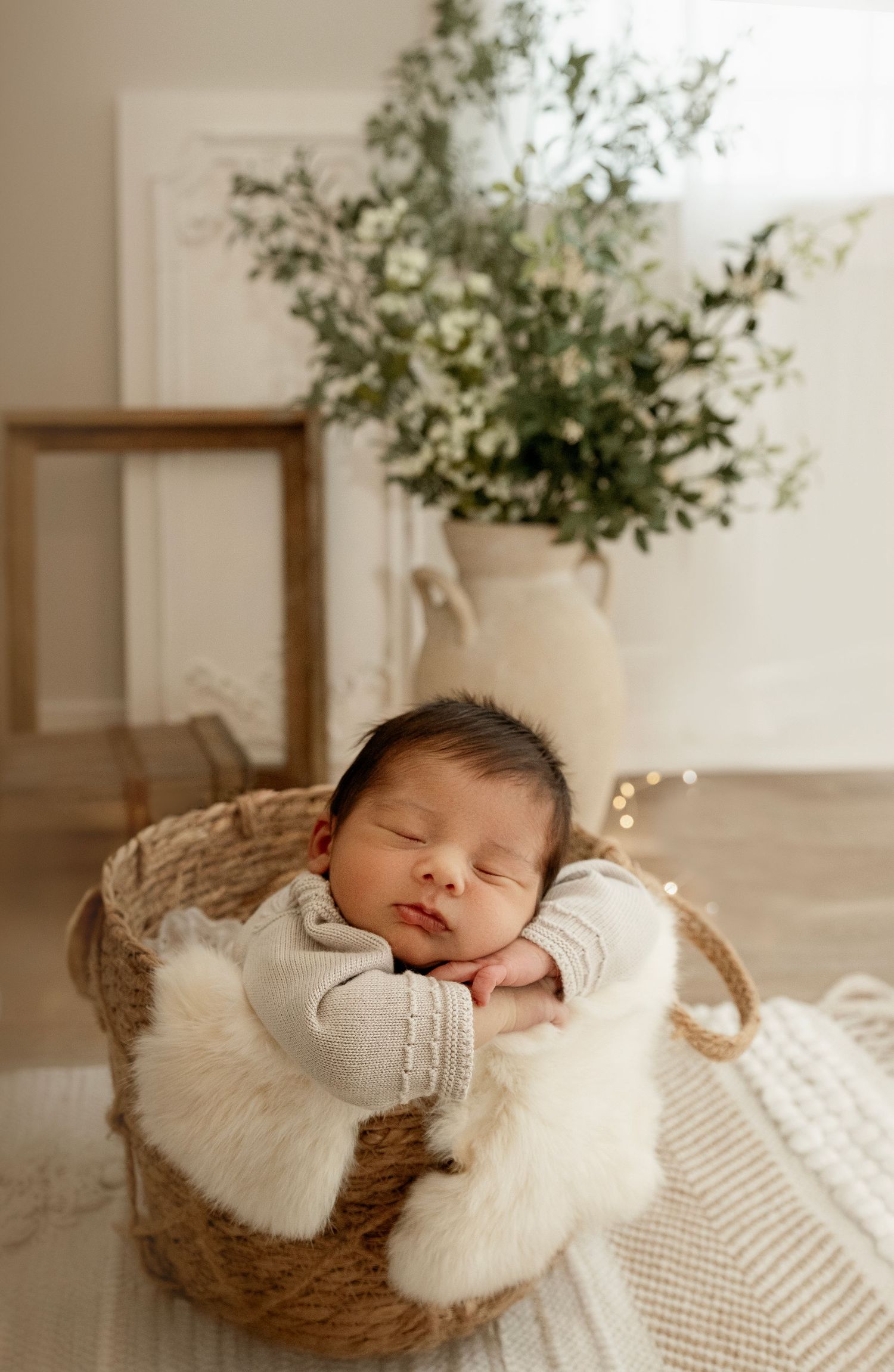 Sleeping baby in cozy white knit outfit rests peacefully in woven basket with soft textured blanket.
