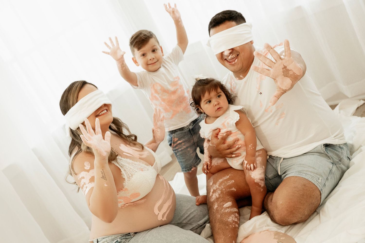 A family in white clothing playfully throws flour while baking together in a bright kitchen.