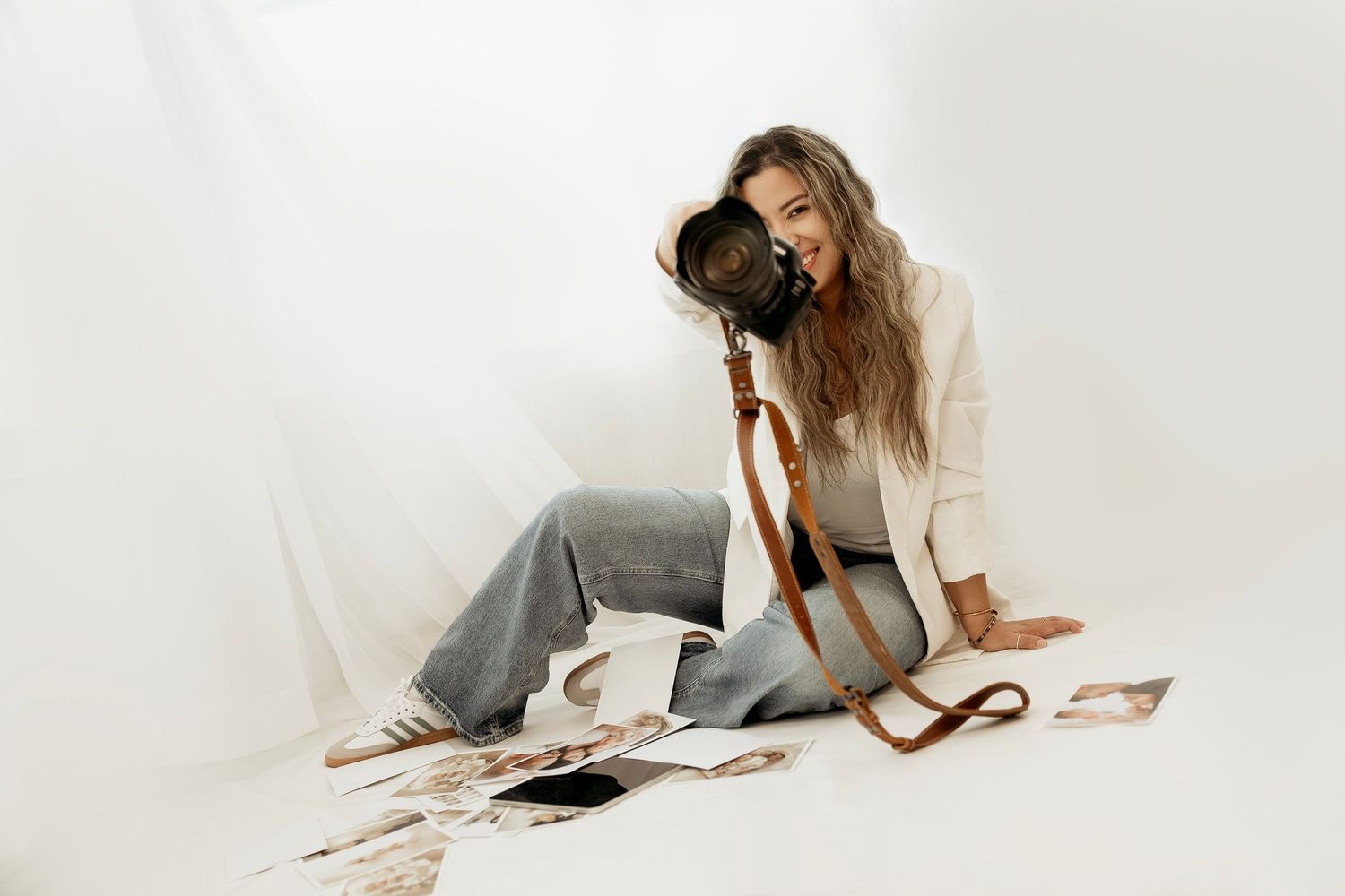 Person sitting on white floor with vintage camera and scattered photographs wearing casual attire and white sweater.