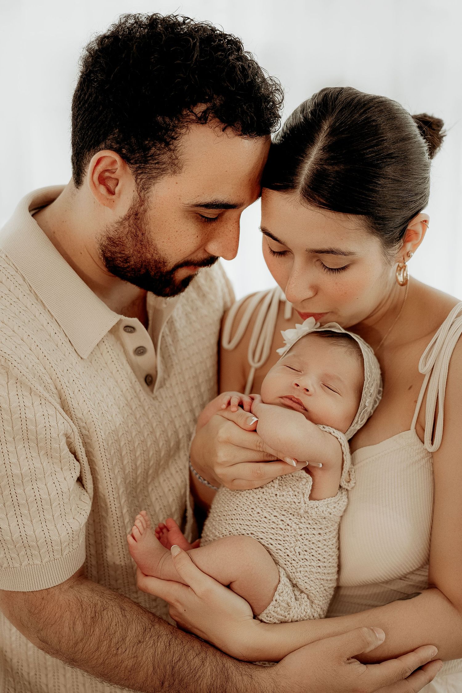 A parent couple shares tender moments with their baby in warm neutral tones during a family photography session.