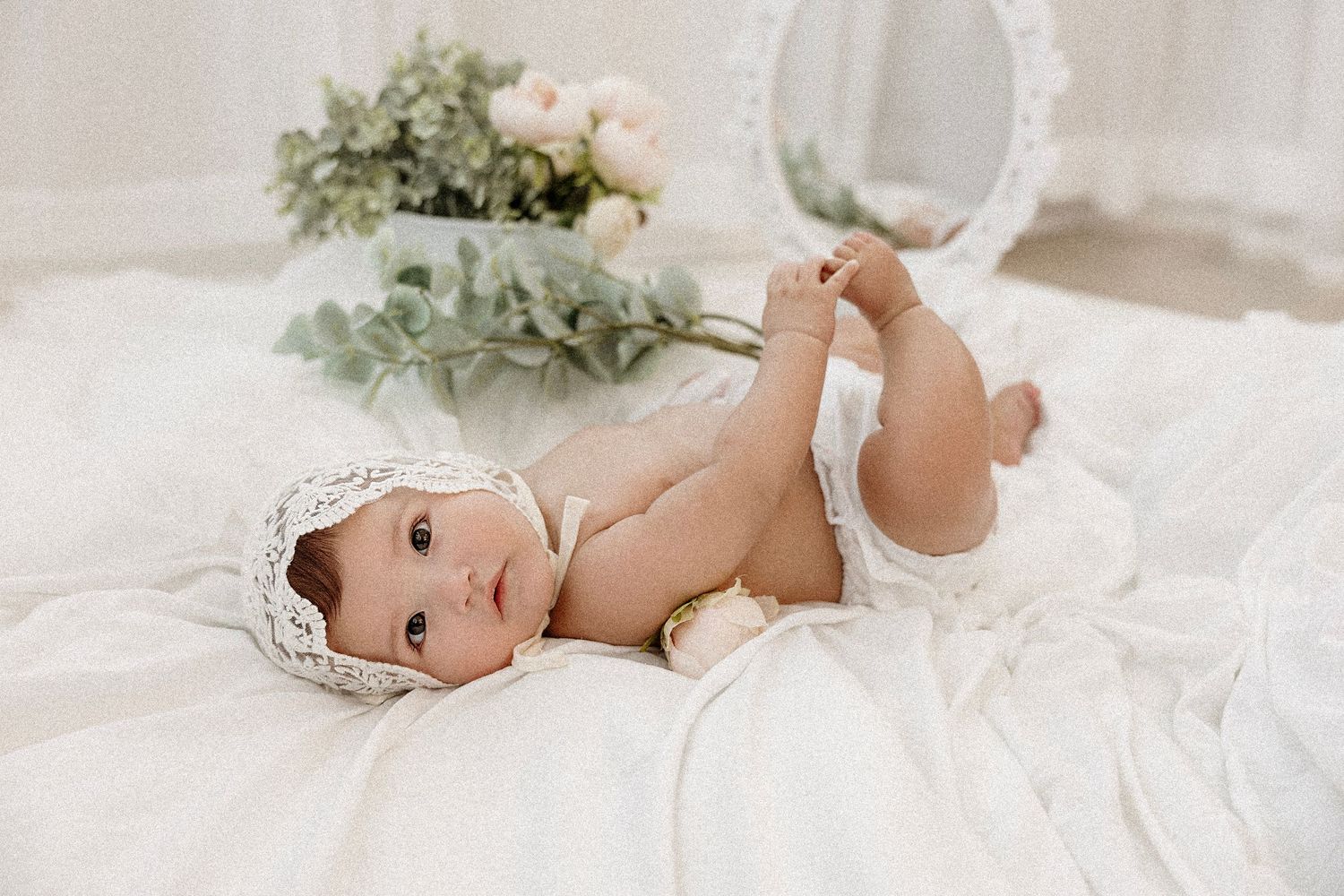 A series of soft and dreamy nursery photographs featuring a baby in white against delicate bedding and floral accents.