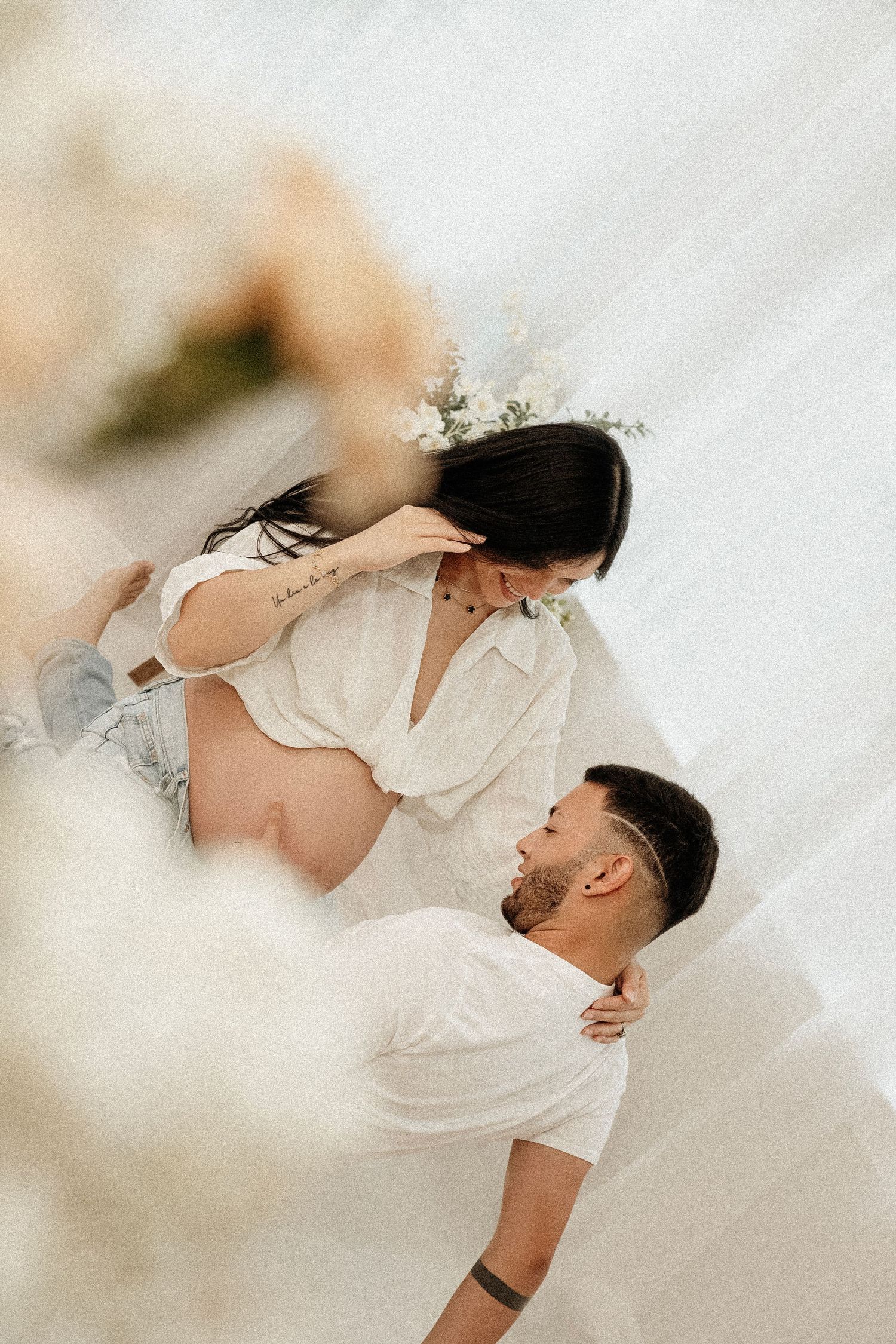 Ethereal couple in white clothing pose intimately together in a dreamy white studio setting.