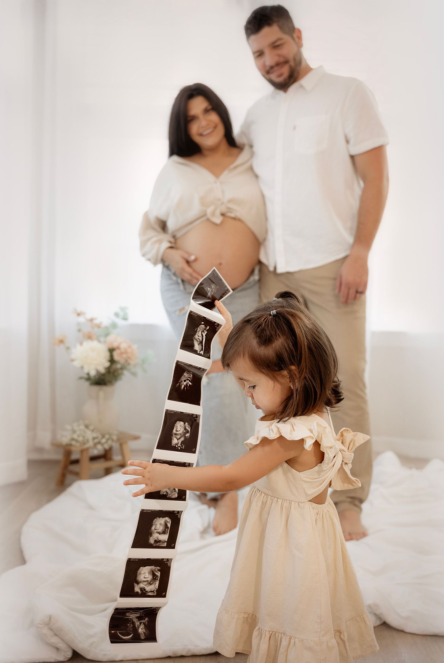A series of ultrasound photos being shared in a bright white room with family members celebrating a pregnancy announcement.