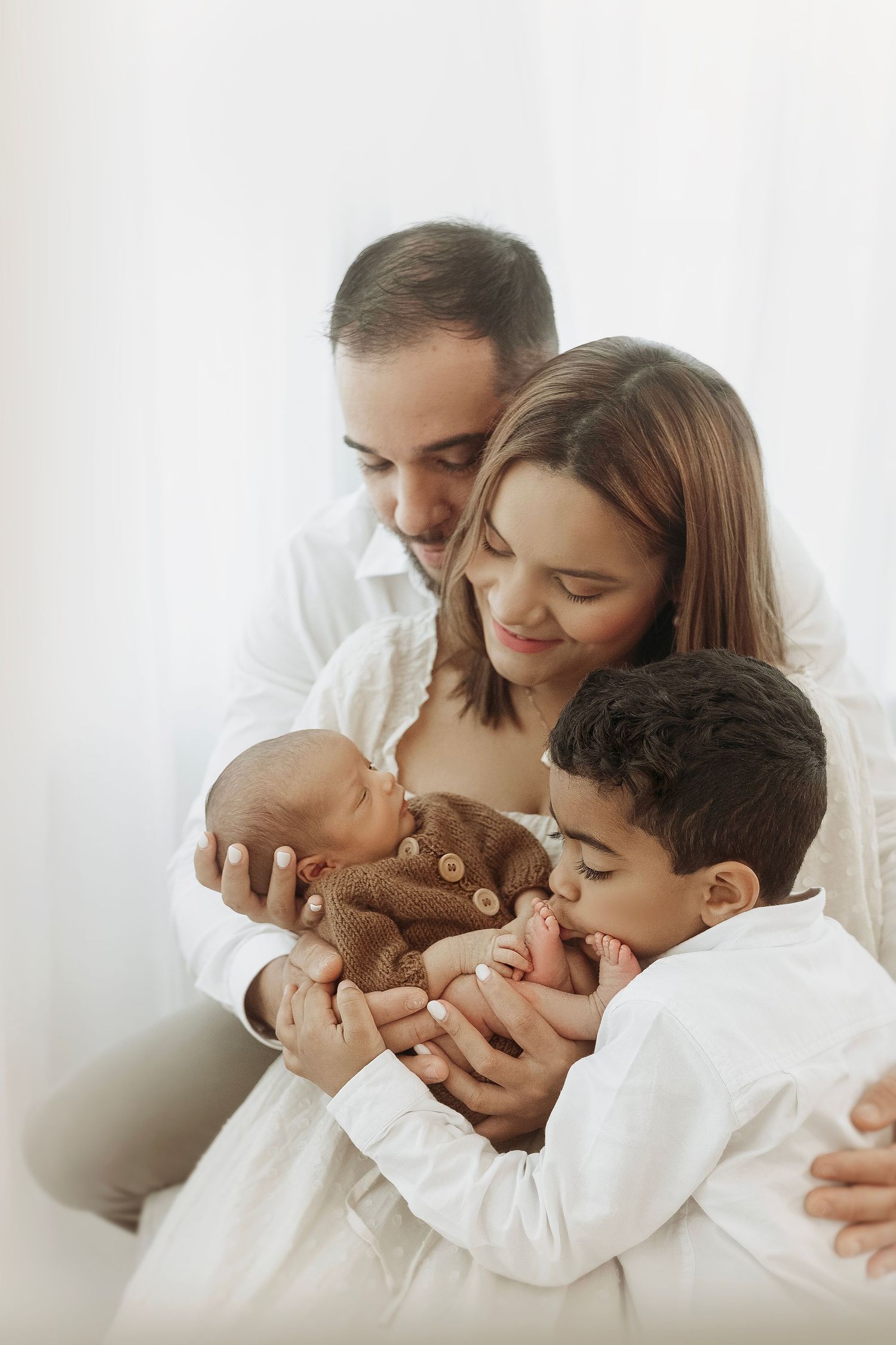A tender family moment captured in a series of soft white photos showing parents embracing their young child.