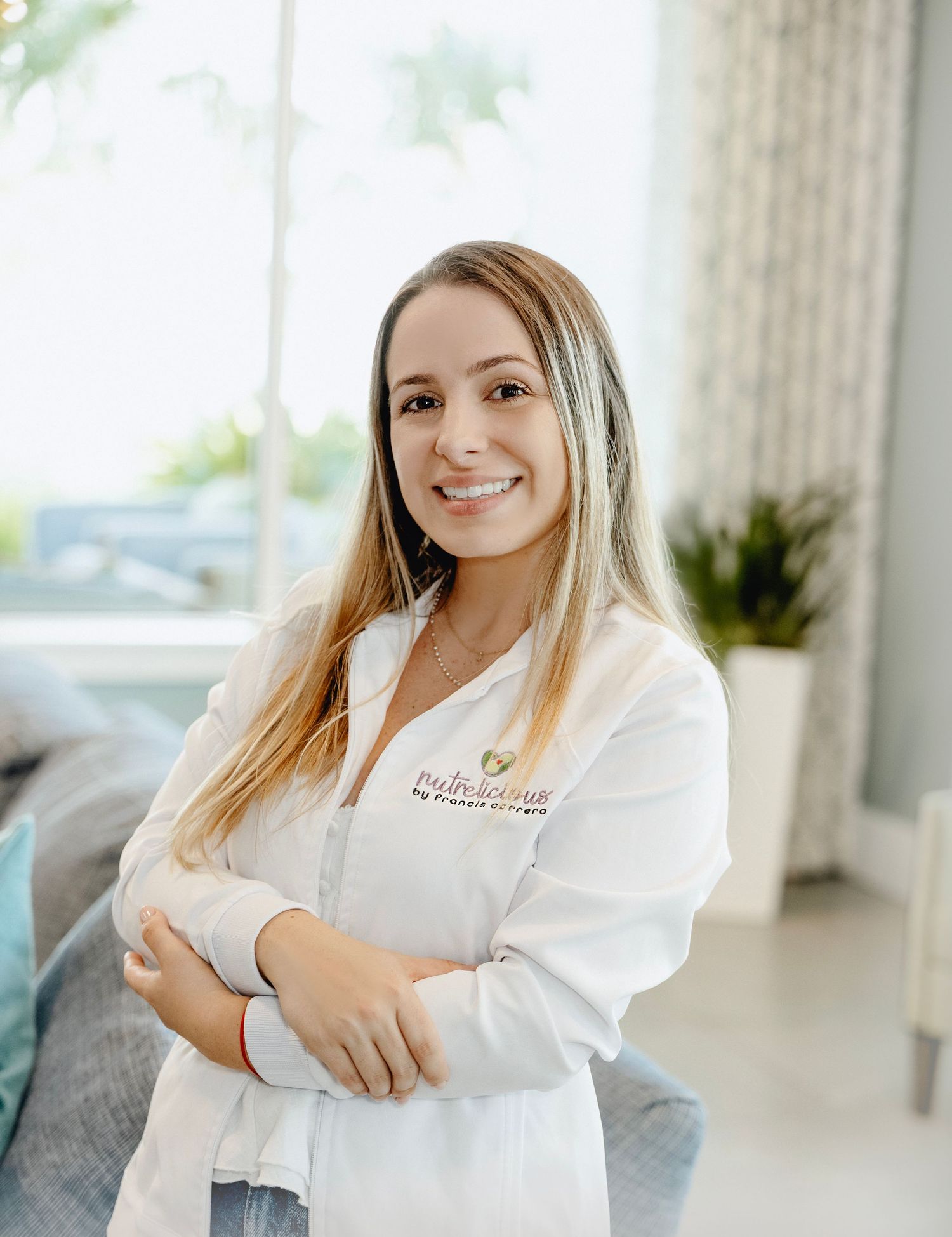 Professional in white attire smiles warmly while posing in a bright modern office setting.