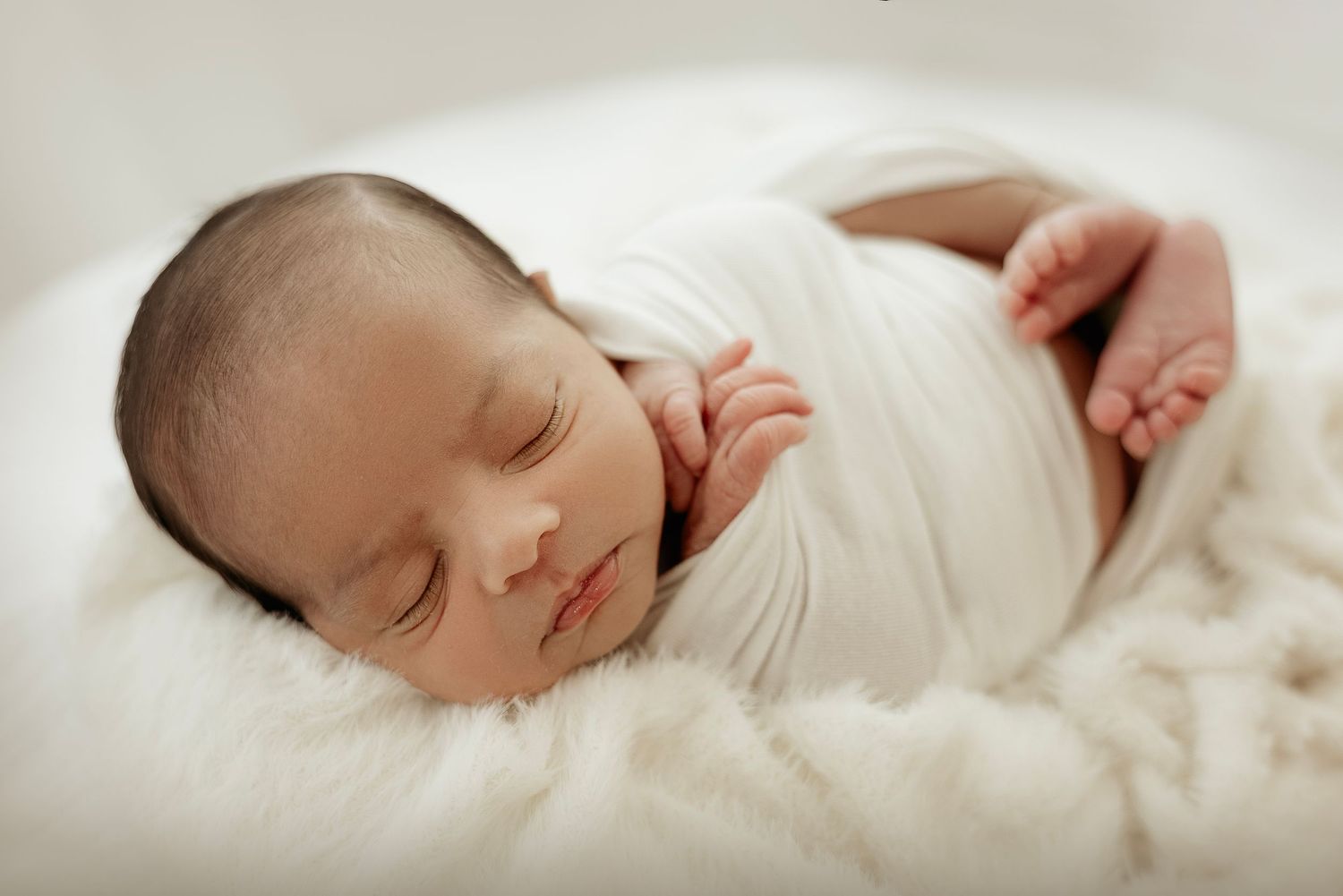 Peaceful newborn baby sleeping soundly wrapped in soft white blankets in a dreamy studio setting.