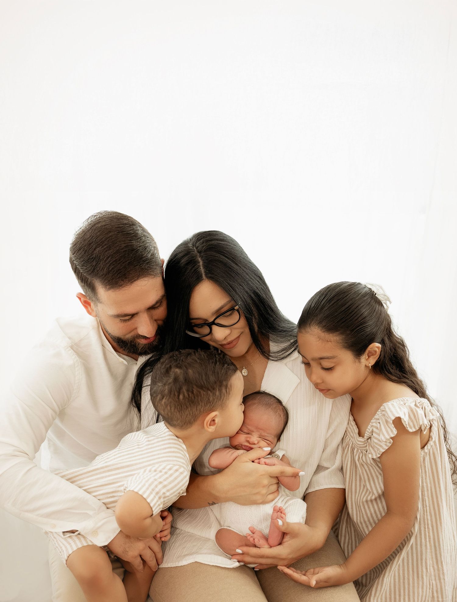 Family with newborn baby wearing white and cream colors together in loving embrace during professional photo shoot.