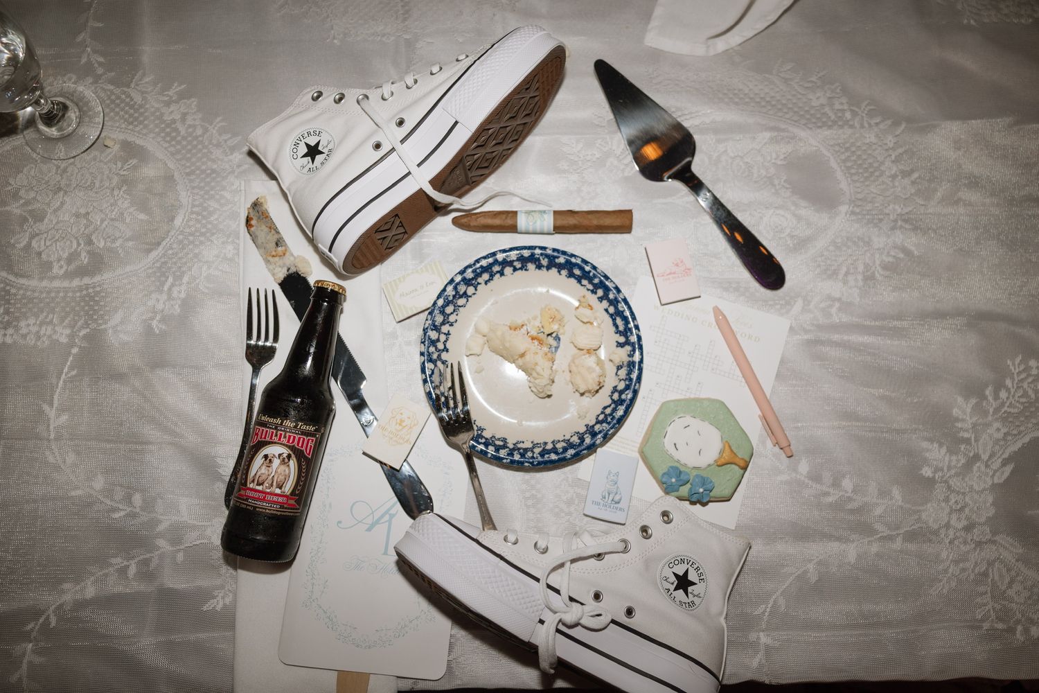Flat lay of wedding keepsakes including Converse sneakers, cake slice, beer bottle, and utensils.
