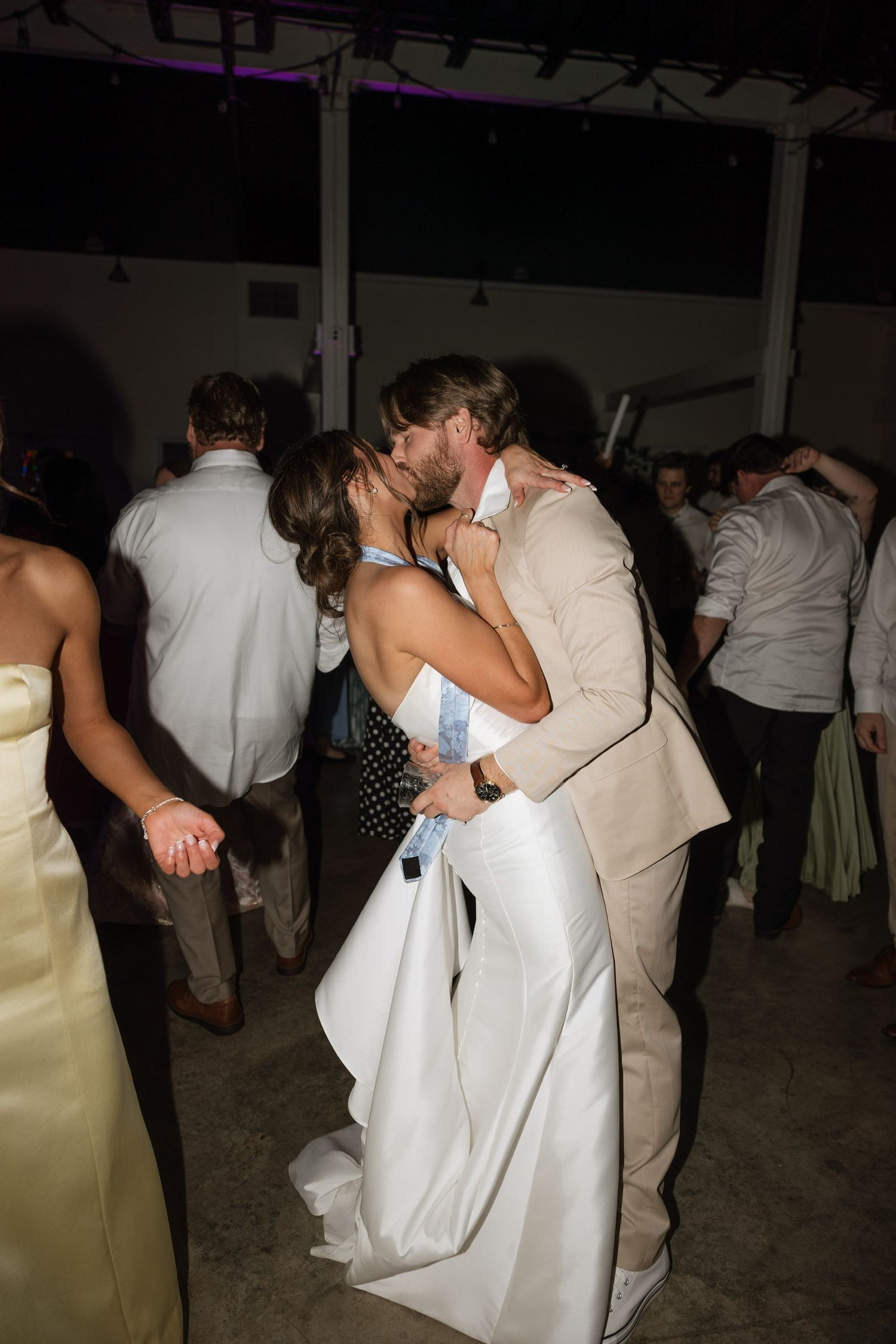 Bride and groom share a romantic kiss on the dance floor surrounded by wedding guests at their reception.