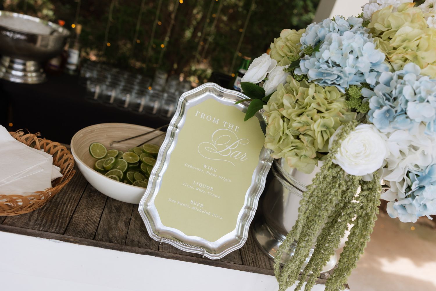Elegant wedding table display with olive green menu card, blue and white hydrangea floral arrangement on rustic wood surface.