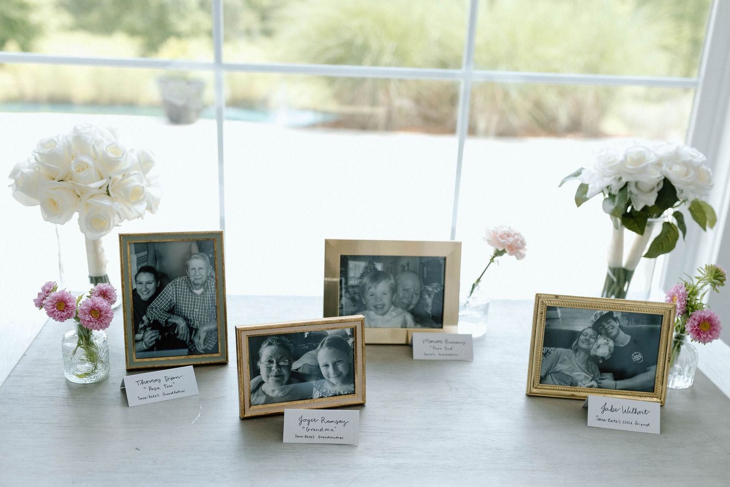 Wedding memory table with gold-framed black and white family photos surrounded by pink and white floral arrangements.