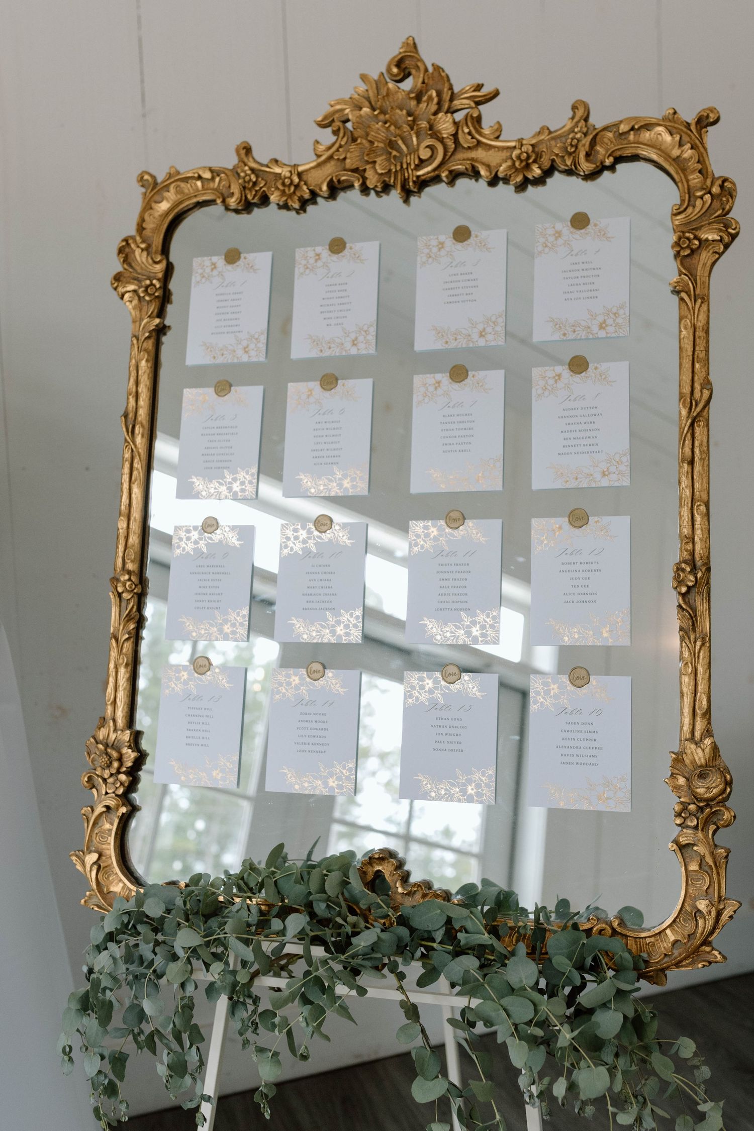 Ornate gold vintage mirror used as wedding seating chart display decorated with eucalyptus greenery.