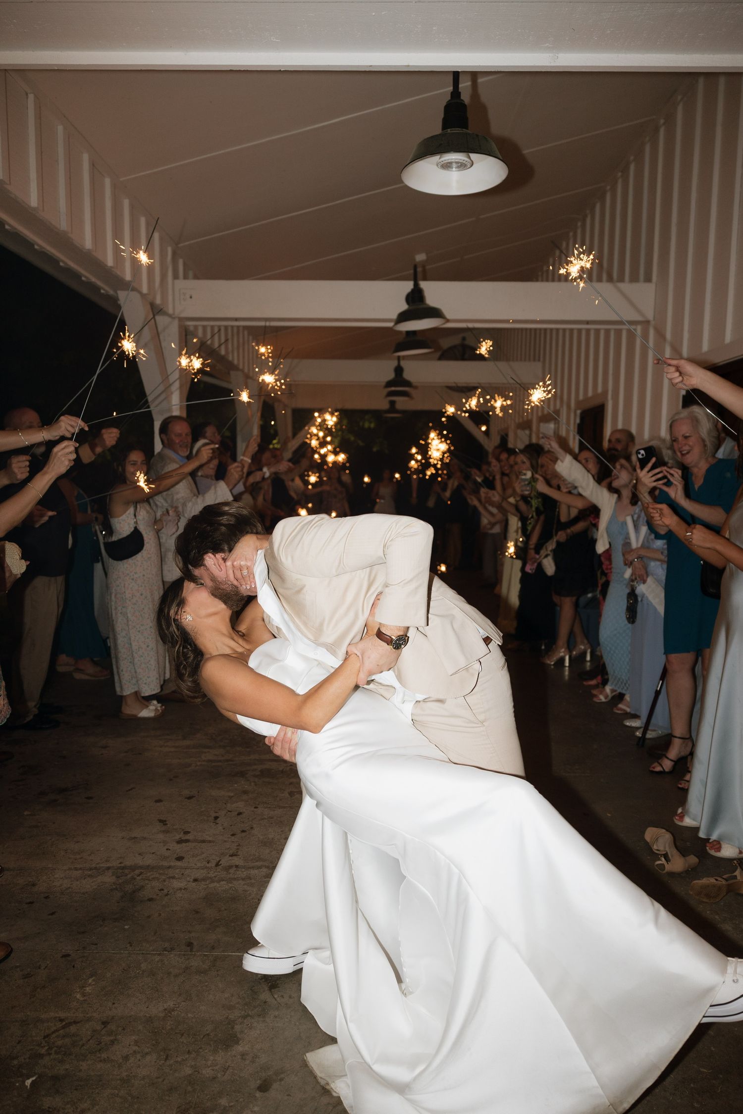 Groom dips bride for romantic kiss during sparkler send-off exit at wedding reception.