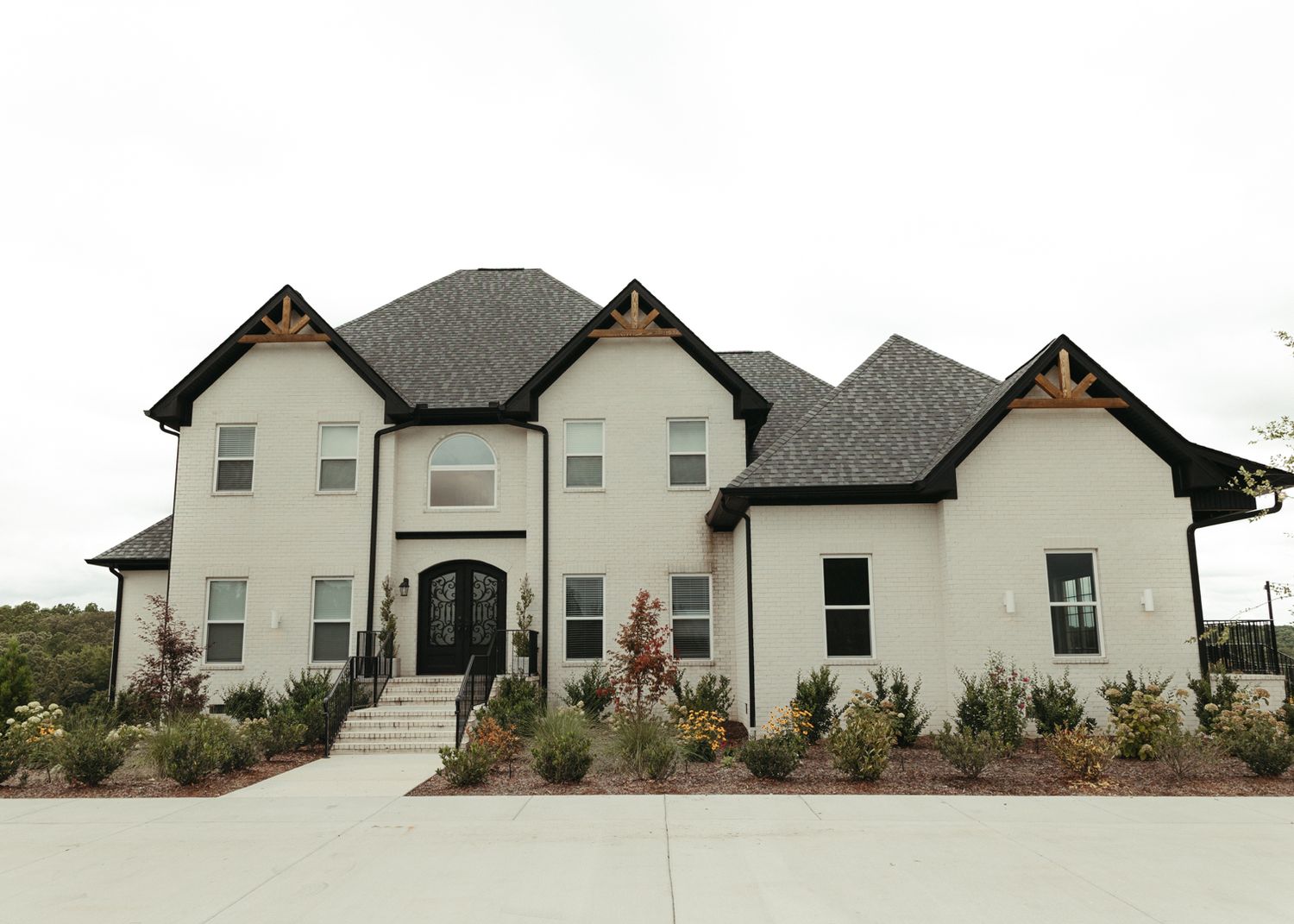 Stunning white brick luxury home with black trim, arched entry door, and manicured landscaping.