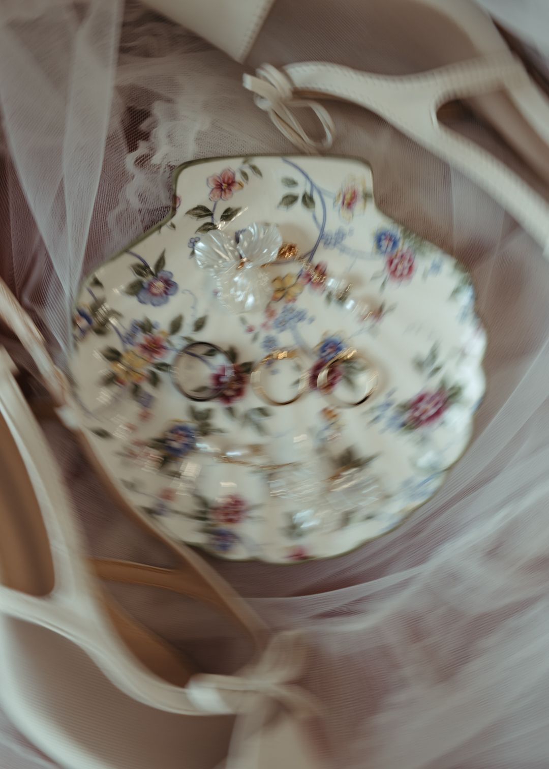Floral ceramic shell dish holding wedding rings on soft tulle fabric.