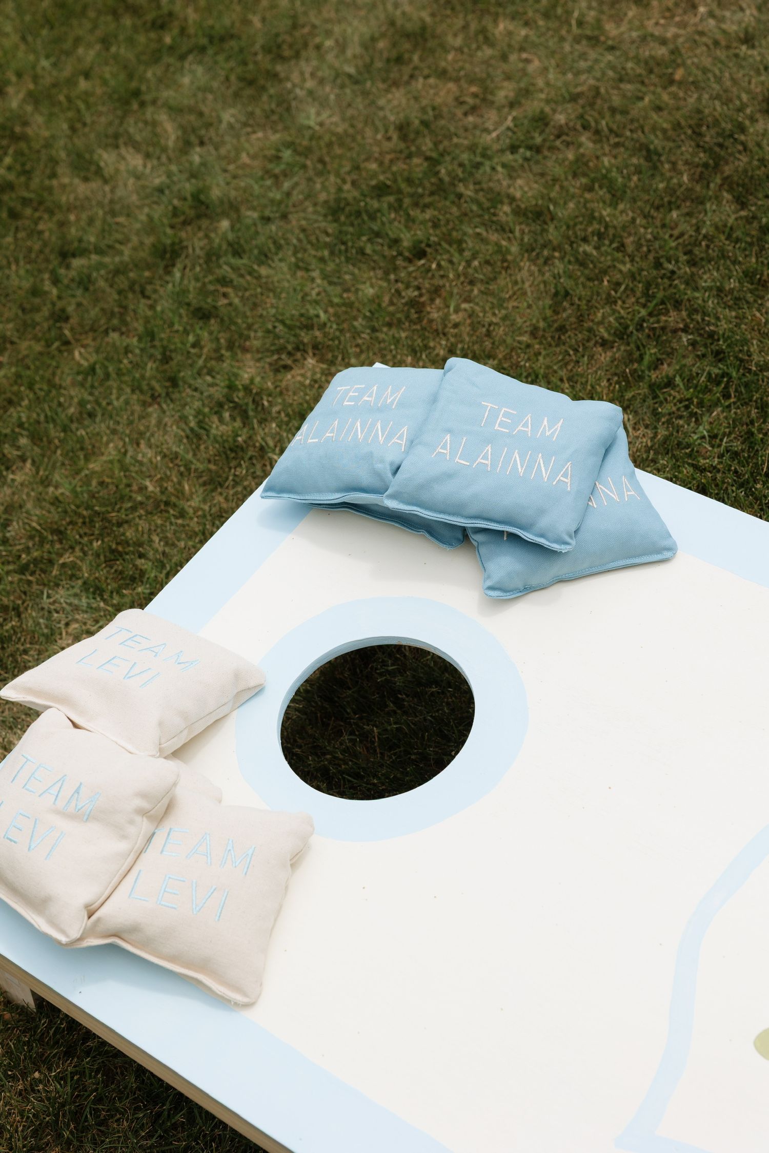 Custom cornhole game board with personalized blue and cream bean bags on green grass.