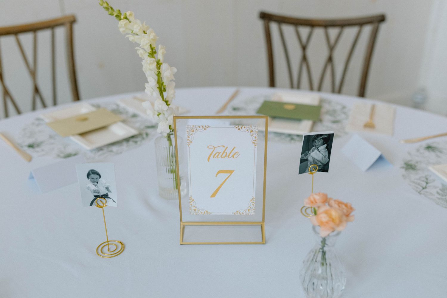 Elegant round wedding reception table with gold Table 7 sign, vintage photos, and delicate floral accents.