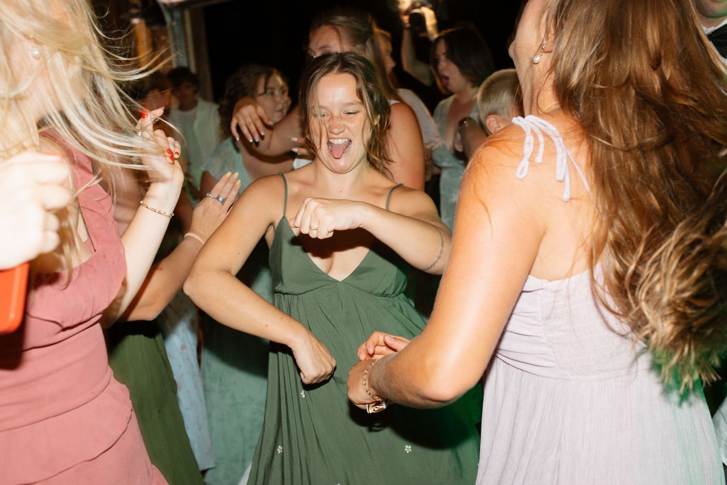 Joyful bridesmaid in green dress dancing enthusiastically with guests at lively wedding reception celebration.