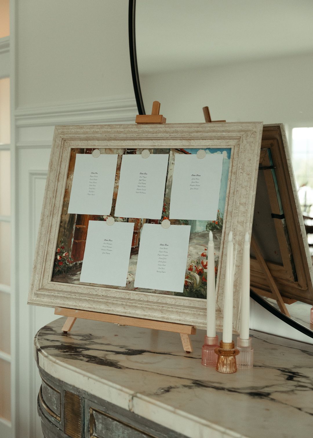 Wedding seating chart displayed in ornate frame on easel atop marble fireplace mantel.