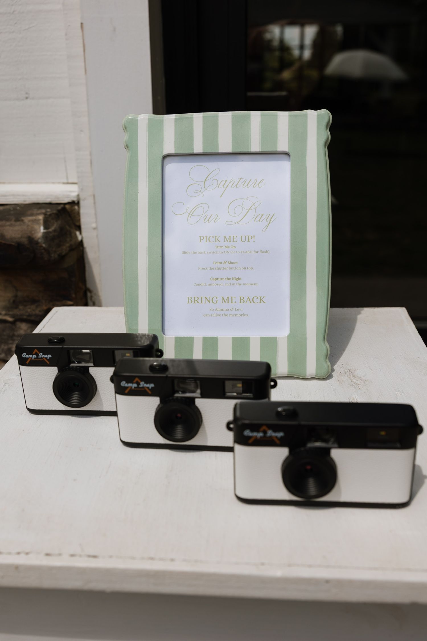 Disposable cameras displayed beside striped frame with Capture Our Day sign at wedding.
