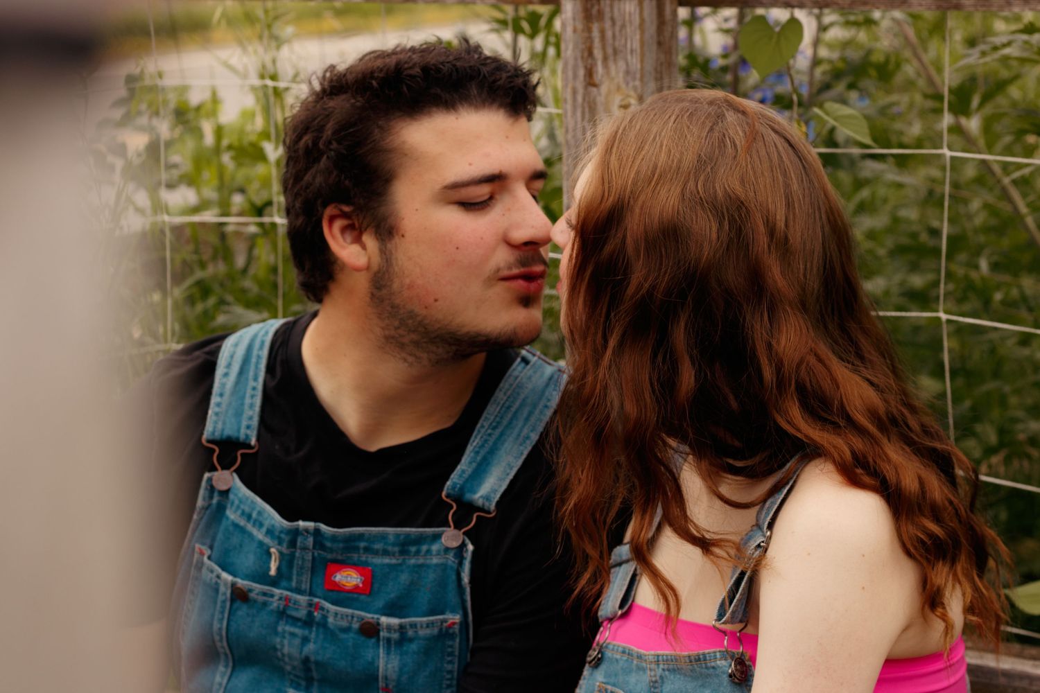 A couple shares an intimate moment on a rustic wooden fence.