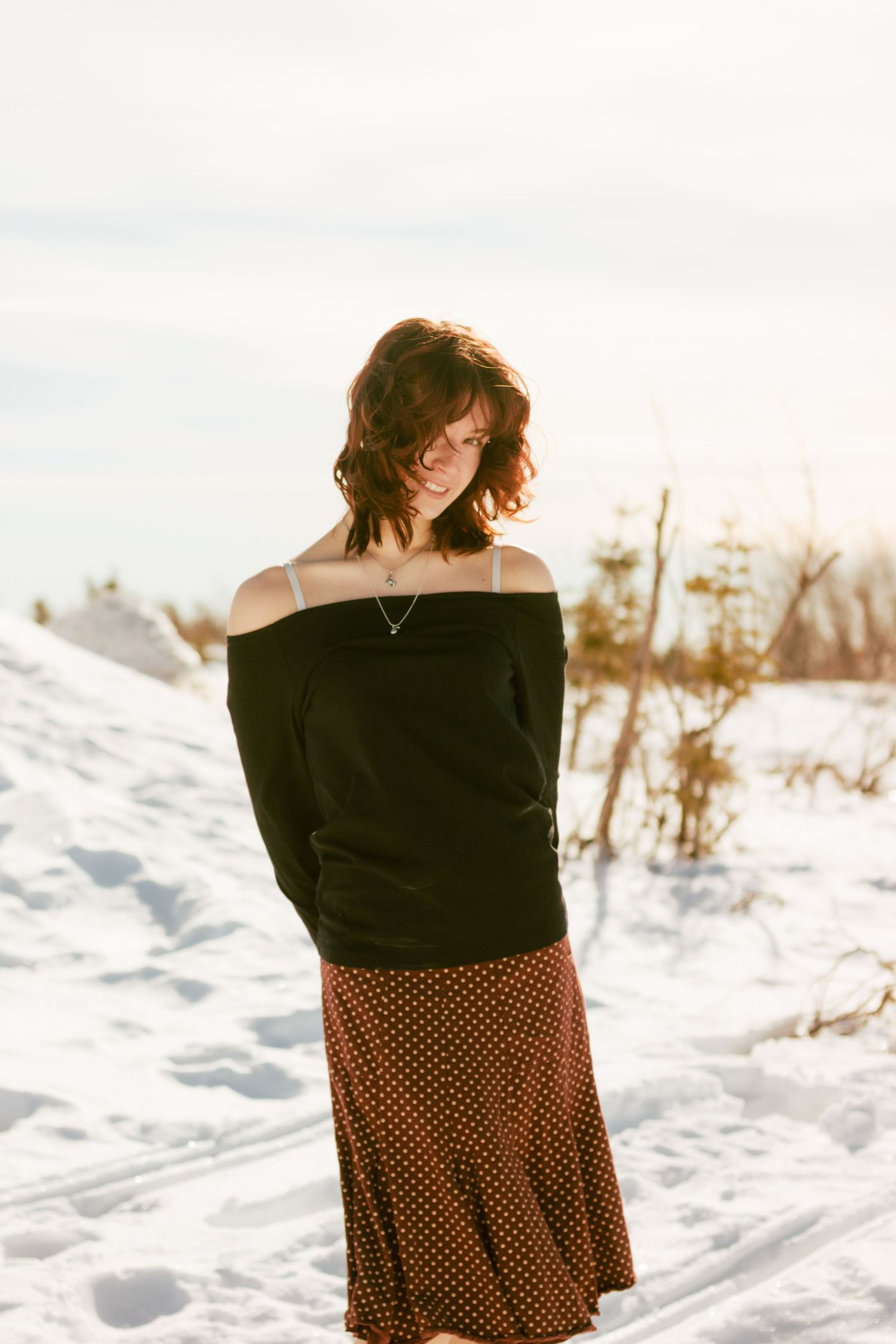 A winter fashion portrait showing an off-shoulder black sweater and polka dot skirt against a snowy landscape.