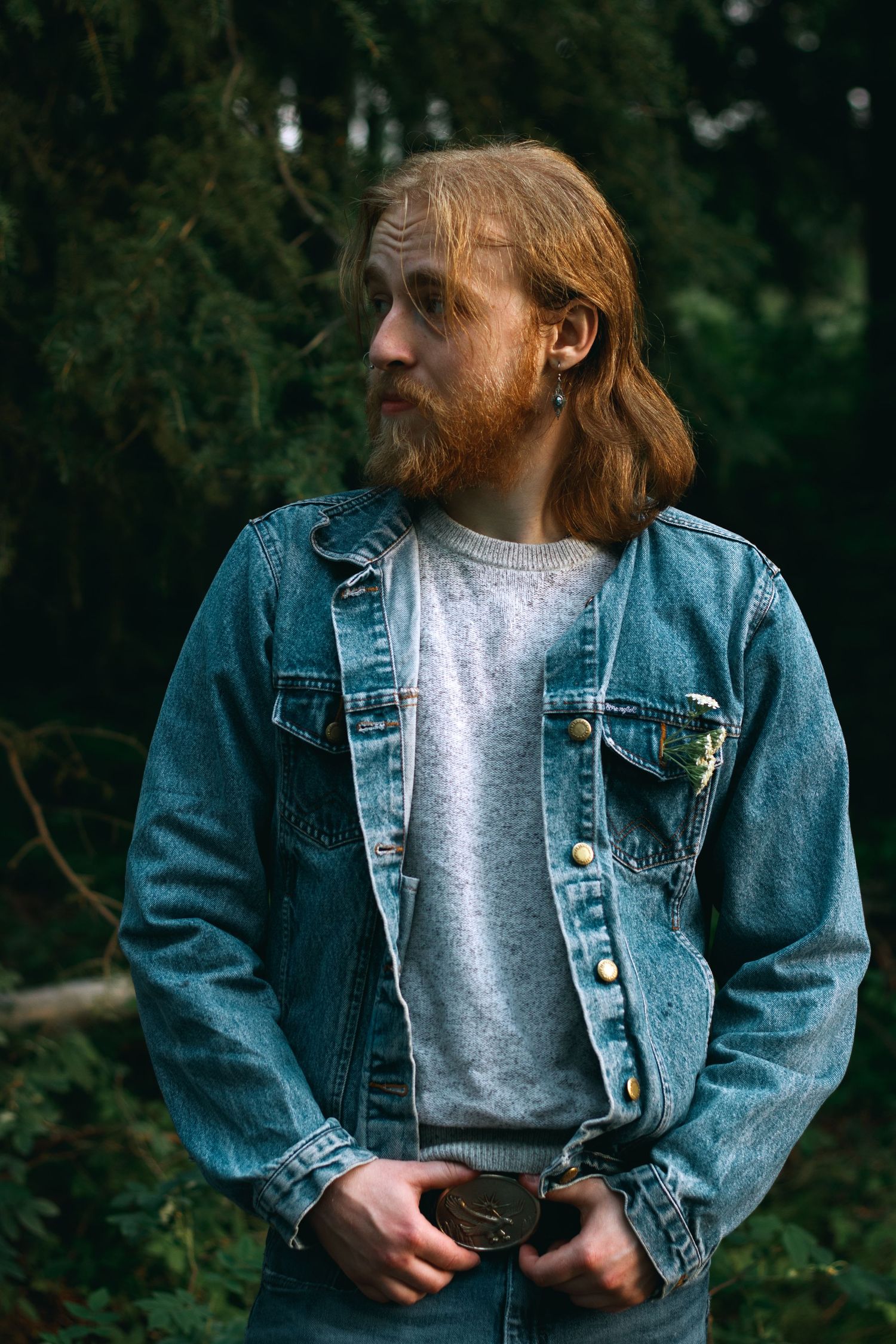 Person wearing denim jacket and grey shirt photographed in natural outdoor setting.