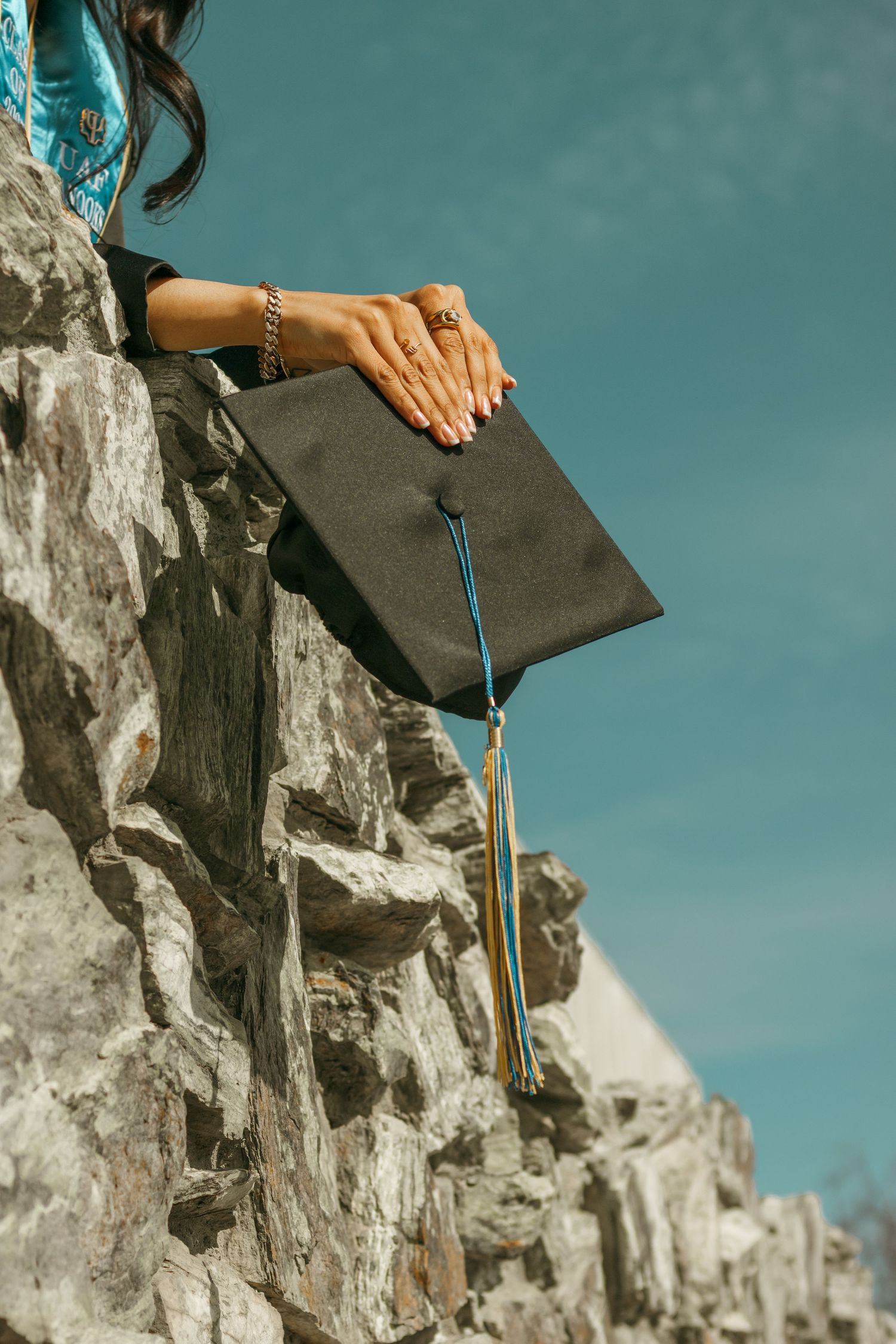 Graduation cap and tassel detail shot against stone architecture and blue sky.