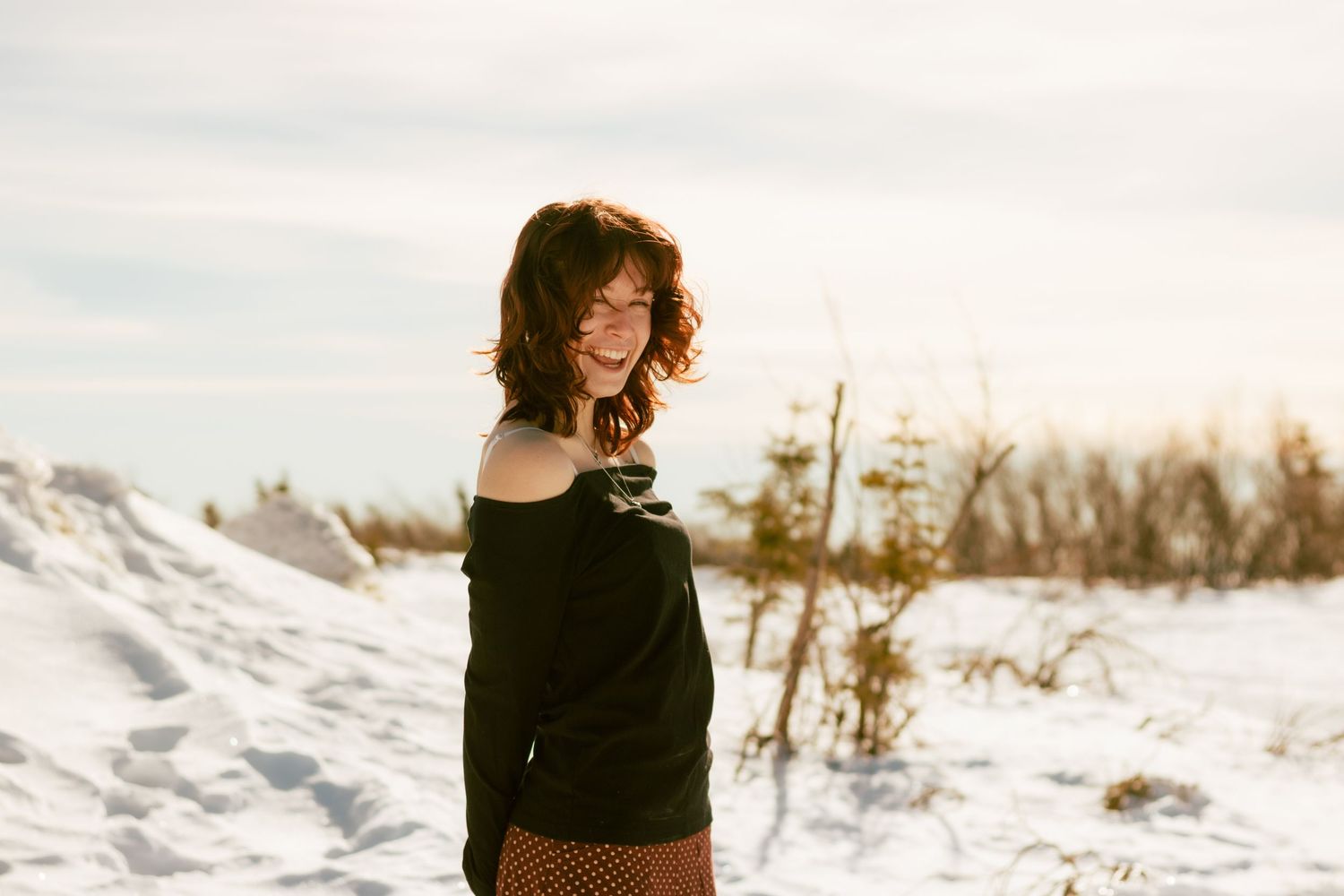 A winter engagement photoshoot shows a couple in a snowy landscape with evergreen trees in the background.