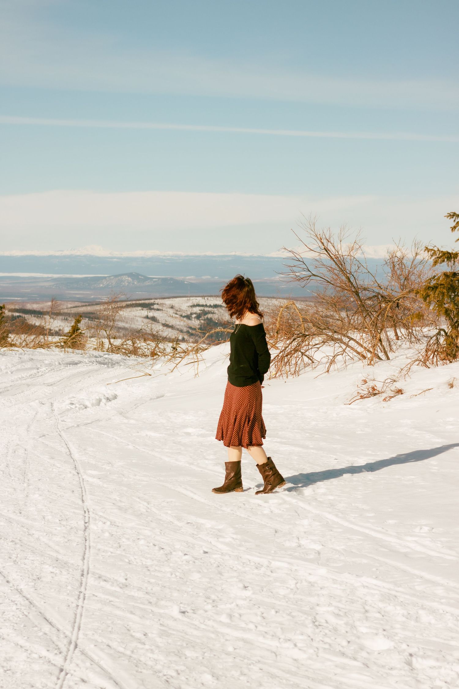 Person walking through a snowy mountain landscape with distant peaks visible in the background.