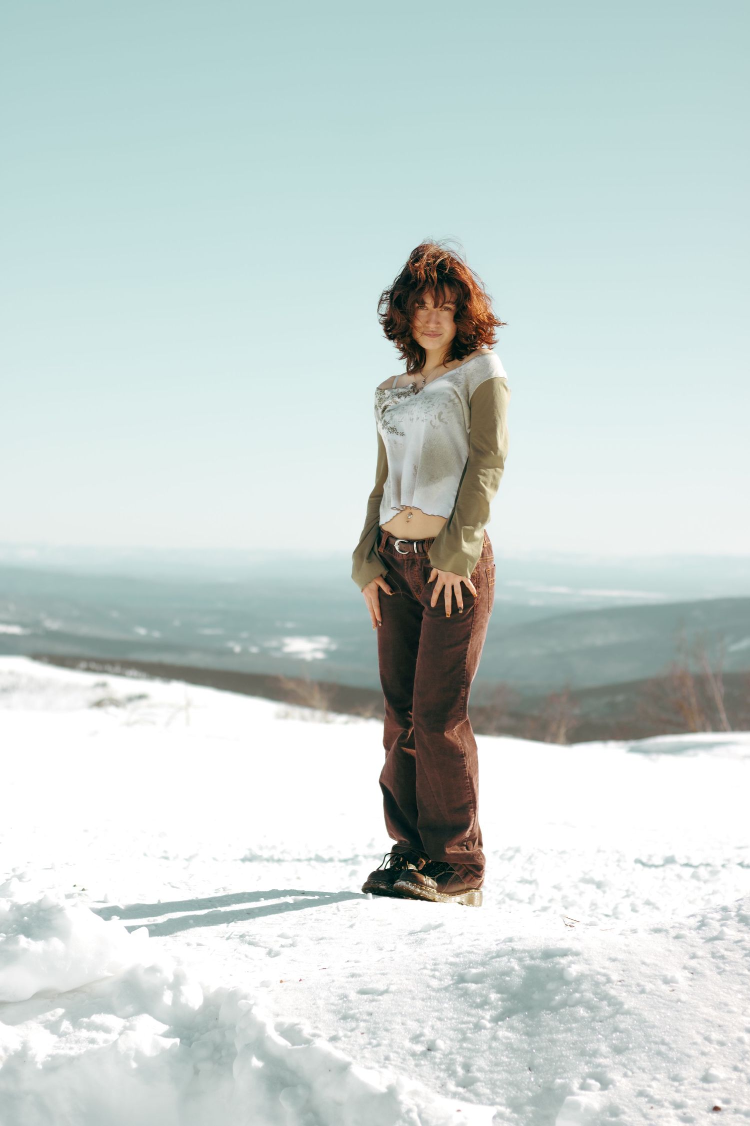 Winter fashion shoot on snowy mountain peak with scenic vista background.