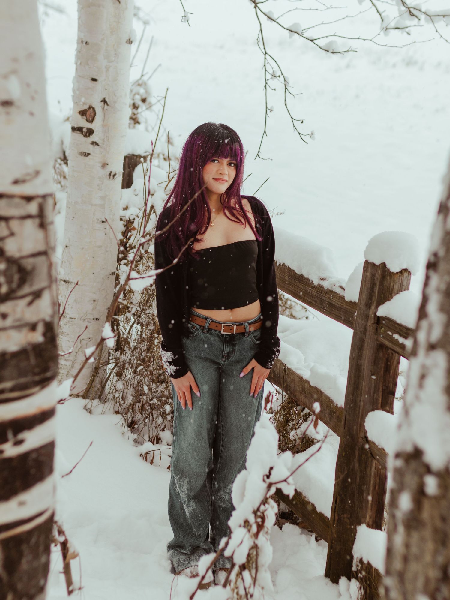 Winter fashion photoshoot in a snowy birch forest with distressed jeans and black top against white bark trees.