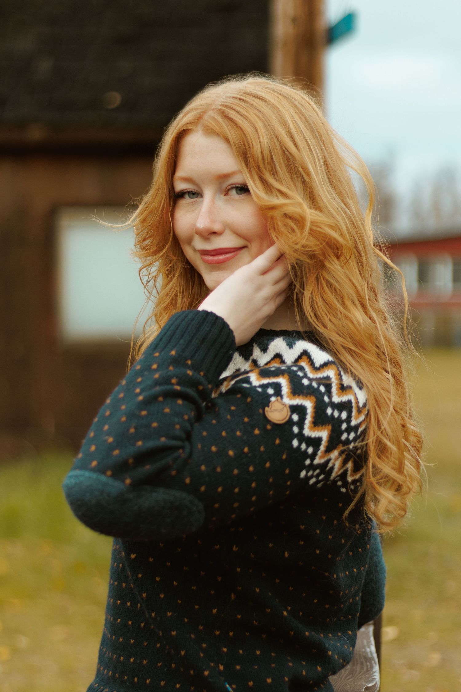 Person in patterned sweater with windswept hair poses outdoors.