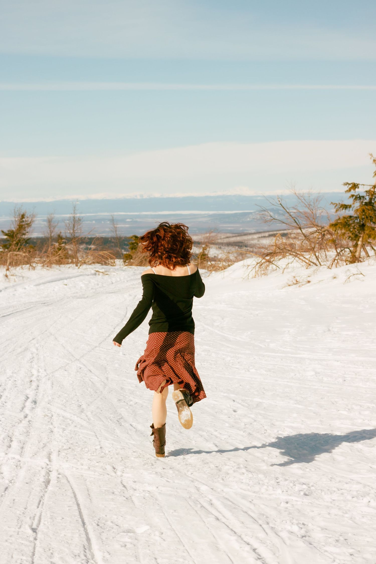 A person jumps across a snowy slope with mountains and blue sky visible in the winter landscape.