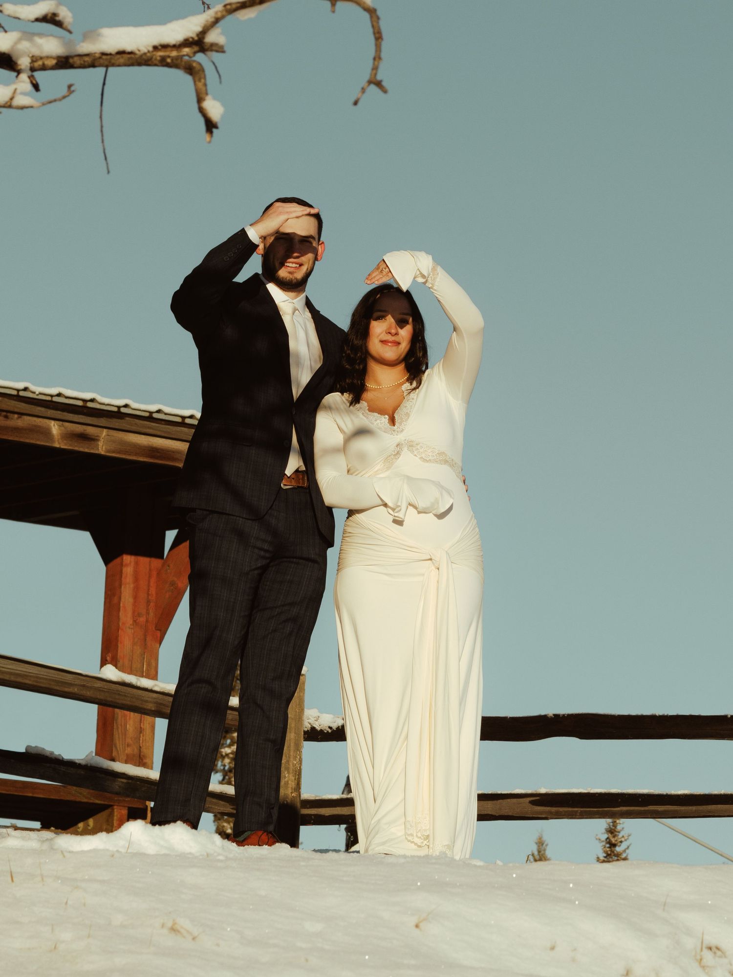 Wedding couple poses in winter scene on snowy hill against pale blue sky.