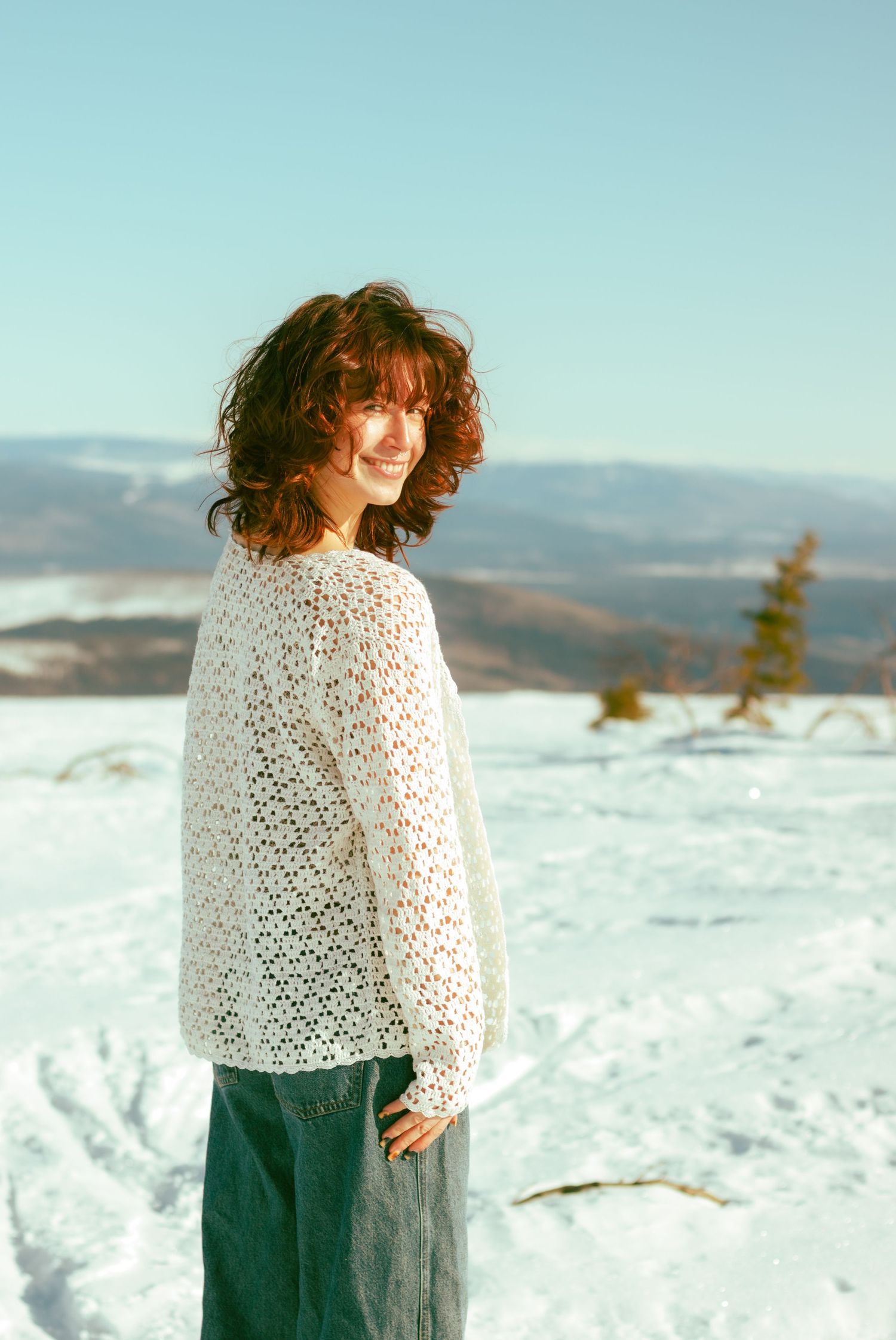 White crochet sweater against snowy winter mountain landscape.