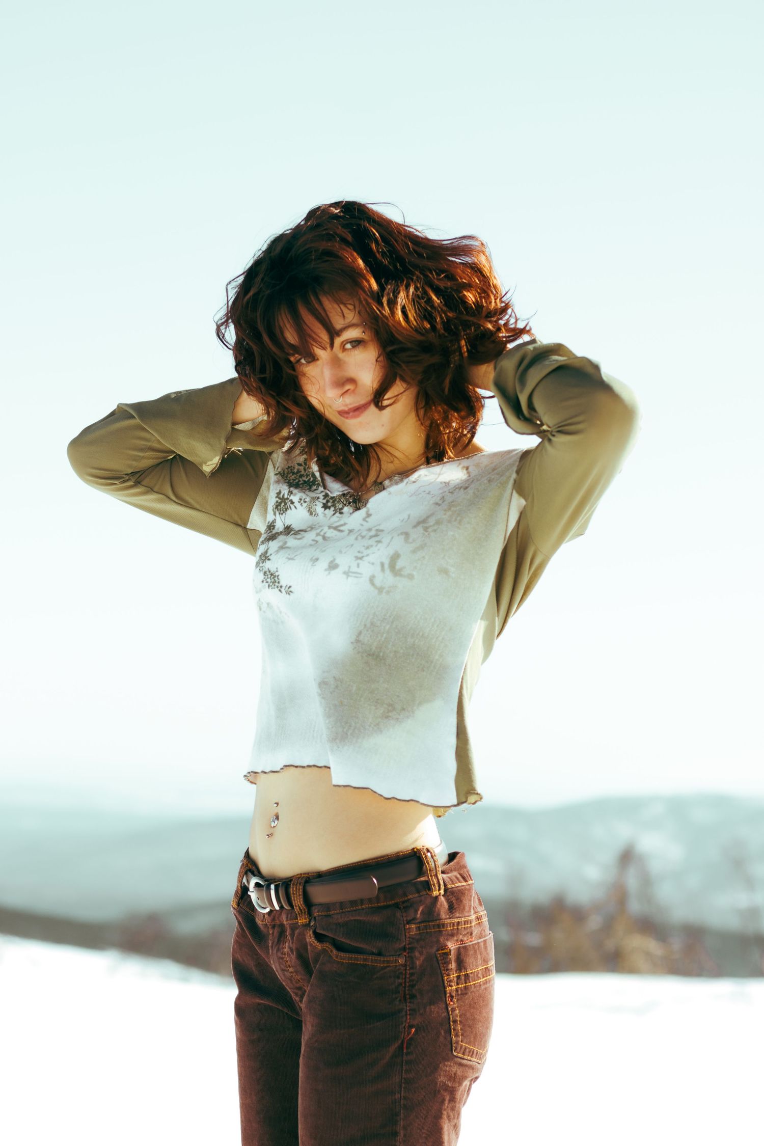 A casual fashion portrait featuring brown corduroy pants and a cropped top against a bright minimalist background.