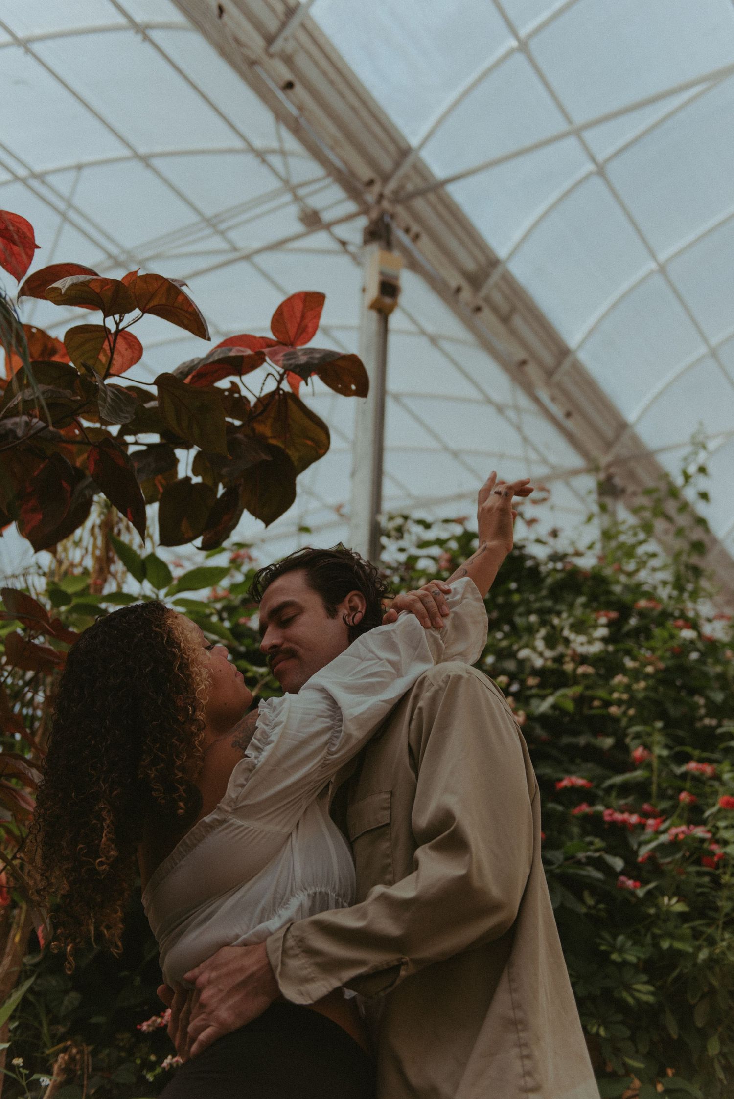 A couple are embracing each other in a green house.