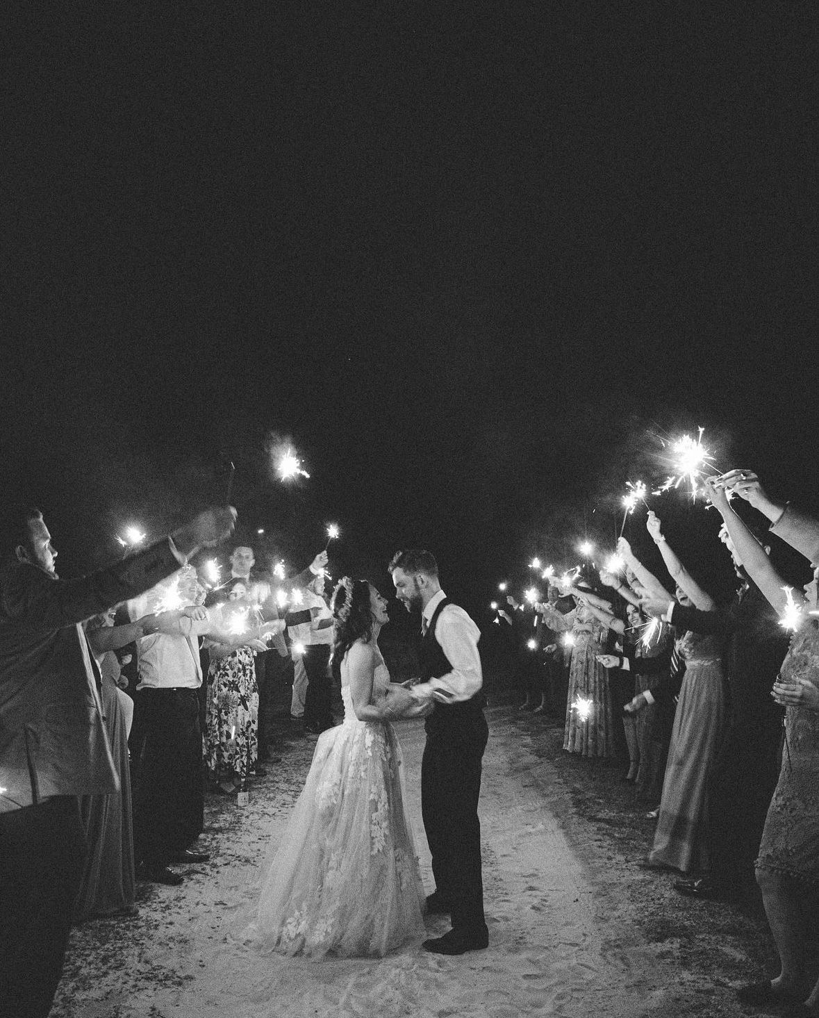 A bride and groom are kissing during their send off with friends and family holding sparklers to celebrate.