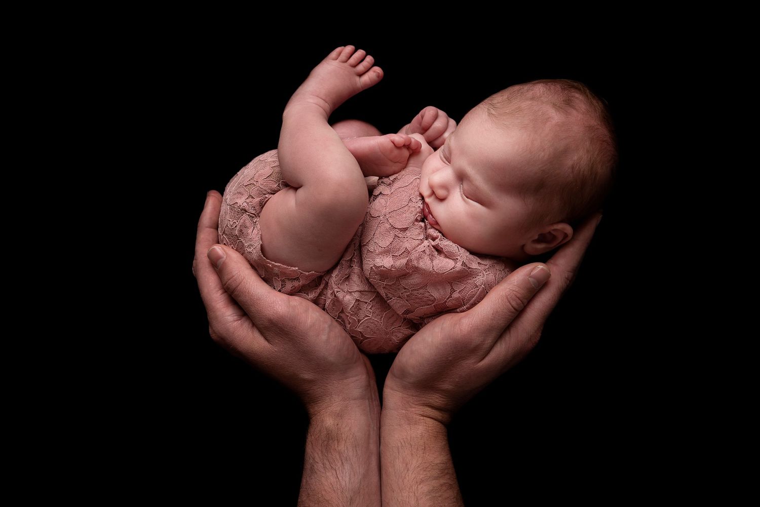 Series of artistic photos showing a newborn baby cradled in gentle hands against dark background.