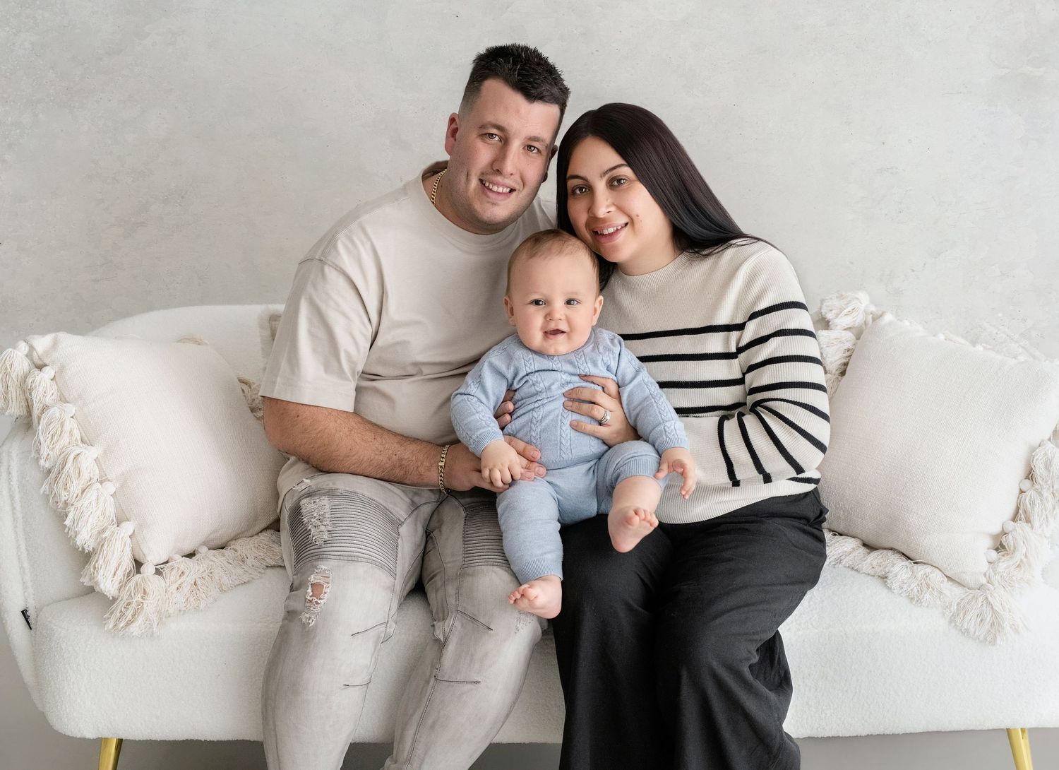 Casual family photos on white couch with baby and parents.