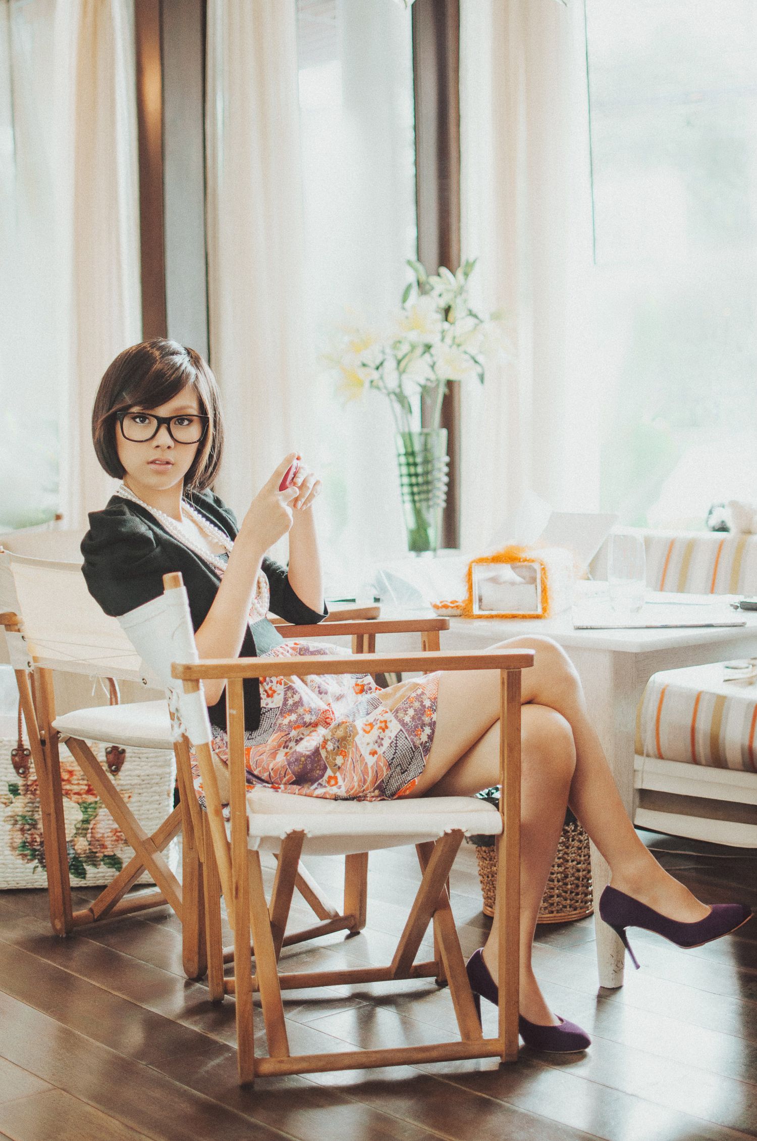 Person in glasses sitting in wooden chair near window with flowers.